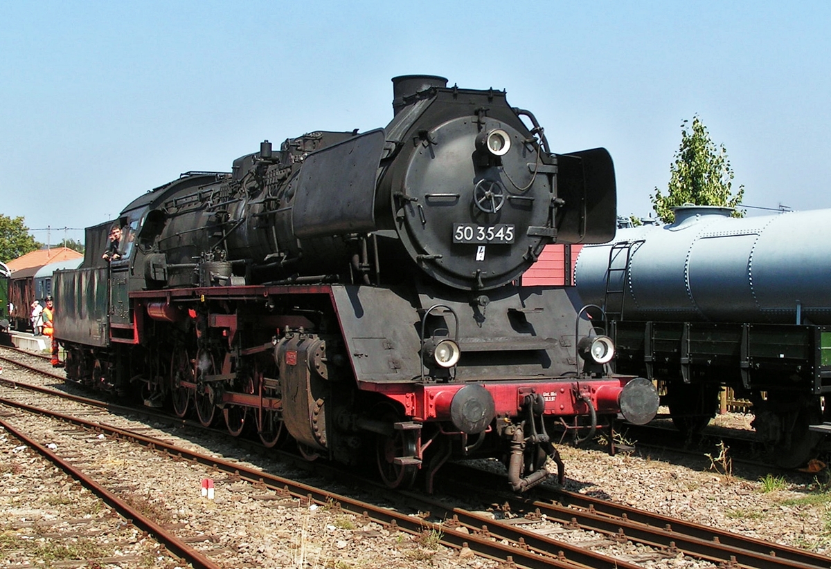 . Am 08.08.2004 setzt die Dampflok 50 3545 im Bahnhof von Losheim am See um, aml�sslich des Dampflok- und Bahnpostfestivals 2004 organisiert vom Museums-Eisenbahn-Club Losheim. (Hans)

Die Geschichte der G�terzuglokomotive 50 3545 der DBK Historische Bahn e.V.:

Die 50 3545 wurde als erste Lokomotive der Baureihe 50 aus dem Baulos der Maschinenfabrik Esslingen 1941 unter der Betriebsnummer 50 1385 abgeliefert. Bei Kriegsende blieb die zur Direktion Hannover z�hlenden Lok in Sachsen-Anhalt stehen und anschlie�end in den Betriebslokpark in der DDR eingereiht. Sie ist ein von vier Lokomotiven aus den Hallen der Maschinenfabrik Esslingen, die in der DDR einer umfassenden Modernisierung unterzogen wurde. Auff�lligstes Merkmal ist dabei der neue Hochleitungskessel mit seinem Mischvorw�rmer auf der Rauchkammer. Von diesen vier Loks blieb neben der 50 3545, wie sie nun genannt wurde, nur noch eine erhalten.

Ab 1970 erhielt die Lok die computergerechte Nummer 50 3545-6. Als eine der wenigen Lokomotiven z�hlte die 50 3545 auch nach der Vereinigung der Deutschen Reichsbahn  der DDR und der Deutschen Bundebahn zur Deutschen Bahn AG zum Betriebsbestand. Die in Wismar beheimatete Lok diente unter der neuen DB-AG-Nummer 050 545-3 als Ausbildungslokomotive. Am 6. Dezember 1995 schied sie – zusammen mit der 52 8134 des Bw Berlin-Pankow (Z-Stellung am, 4.12.1994) - als letzte Staatsbahn-Dampflokomotive aus dem aktiven Dienst.

Die Lok wurde von der DBK Historischen Bahn Verein im Sommer 1996 ab Standort Meiningen erworben und nach Abschluss der Hauptuntersuchung im Dampflokwerk Meiningen ab April 1997 eingesetzt. Immer wiederkehrende Lagersch�den zwangen den Verein, die Lok im Herbst 1999 nach einem erneuten Lagerschaden, vorerst abzustellen. Nach umfangreichen Fahrwerksreparaturen wurde die Lok inkl. einer Kesselhauptuntersuchung im Mai 2002 wieder in Betrieb genommen. Danach stand die Lok dem Verein jahrelang zuverl�ssig zur Verf�gung und kam bei ihren vielen Sonderfahrten um Einsatz. Am 4. Dezember 2005 erlitt die Lok auf Grund eines Wasserschlages leider einen schweren Triebwerkschaden und ist seither in Crailsheim konserviert abgestellt. Ihre Reparatur bzw. Wiederinbetriebnahme ist derzeit nicht geplant. 

Die technischen Daten der 50 3545:

Baujahr: 1942
Leistung: 1650 PS
H�chstgeschwindigkeit: 80 km/h
Wasser: 26 m�
Kohle: 8 Tonnen
HU-Abnahme: 11.05.2005
Fristablauf: Abgestellt wegen Triebwerkschaden
Hersteller: Maschinenfabrik Esslingen
