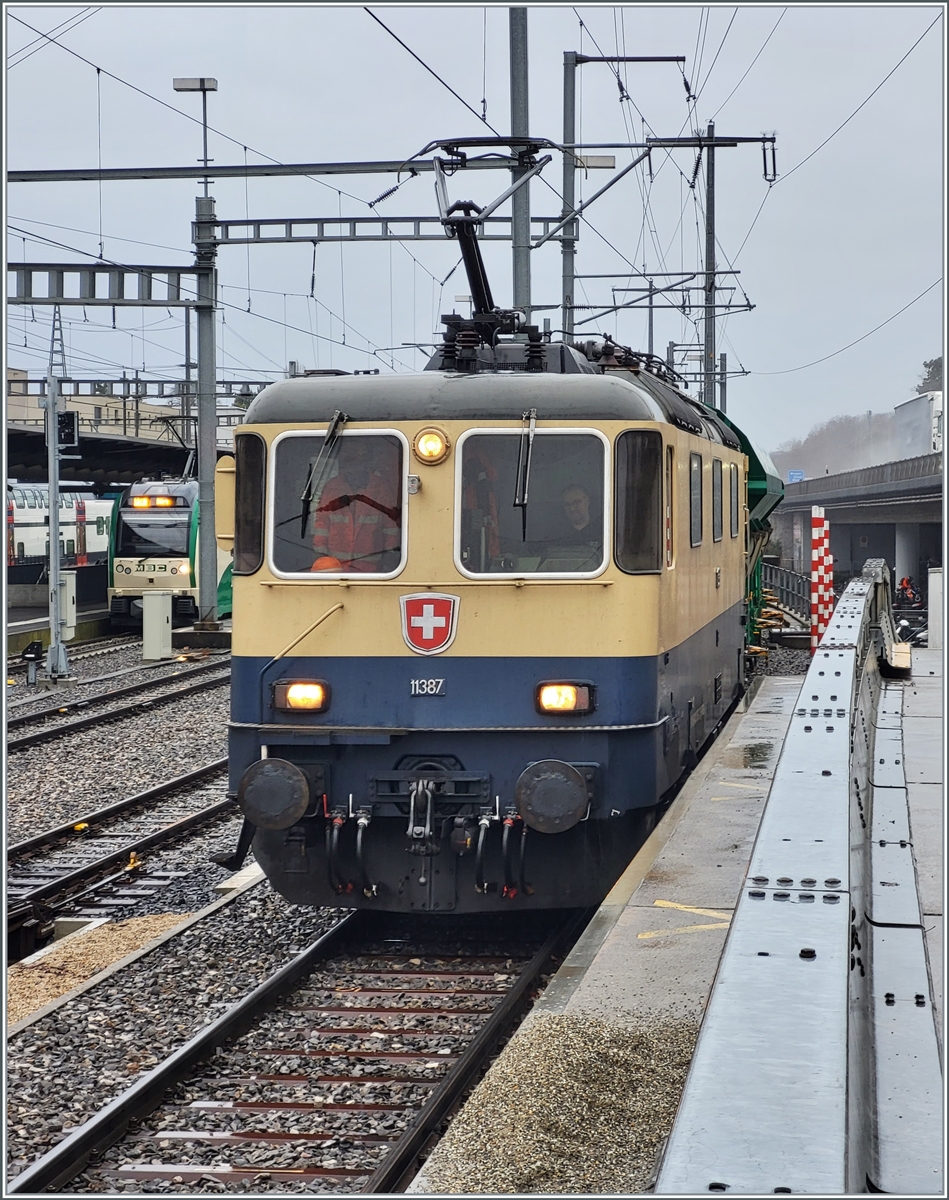 Da die BAM /MBC eigene Re 4/4 II 506 (Re 420 506) zur Zeit in der Revision in Bellinzona weilt, hat die BAM MBC die IRSI/IGE  Rheingold  Re 4/4 II 11387 (Re 421 387-2) angemietet. Die Lok trägt die UIC Nummer Re 421 91 885 4421 387-2 CH-IRSI. Das Bild zeigt die Lok beim schieben ihres Zugs Gland - Apples auf die Rollbockanlage in Morges. 

22. Februar 2024