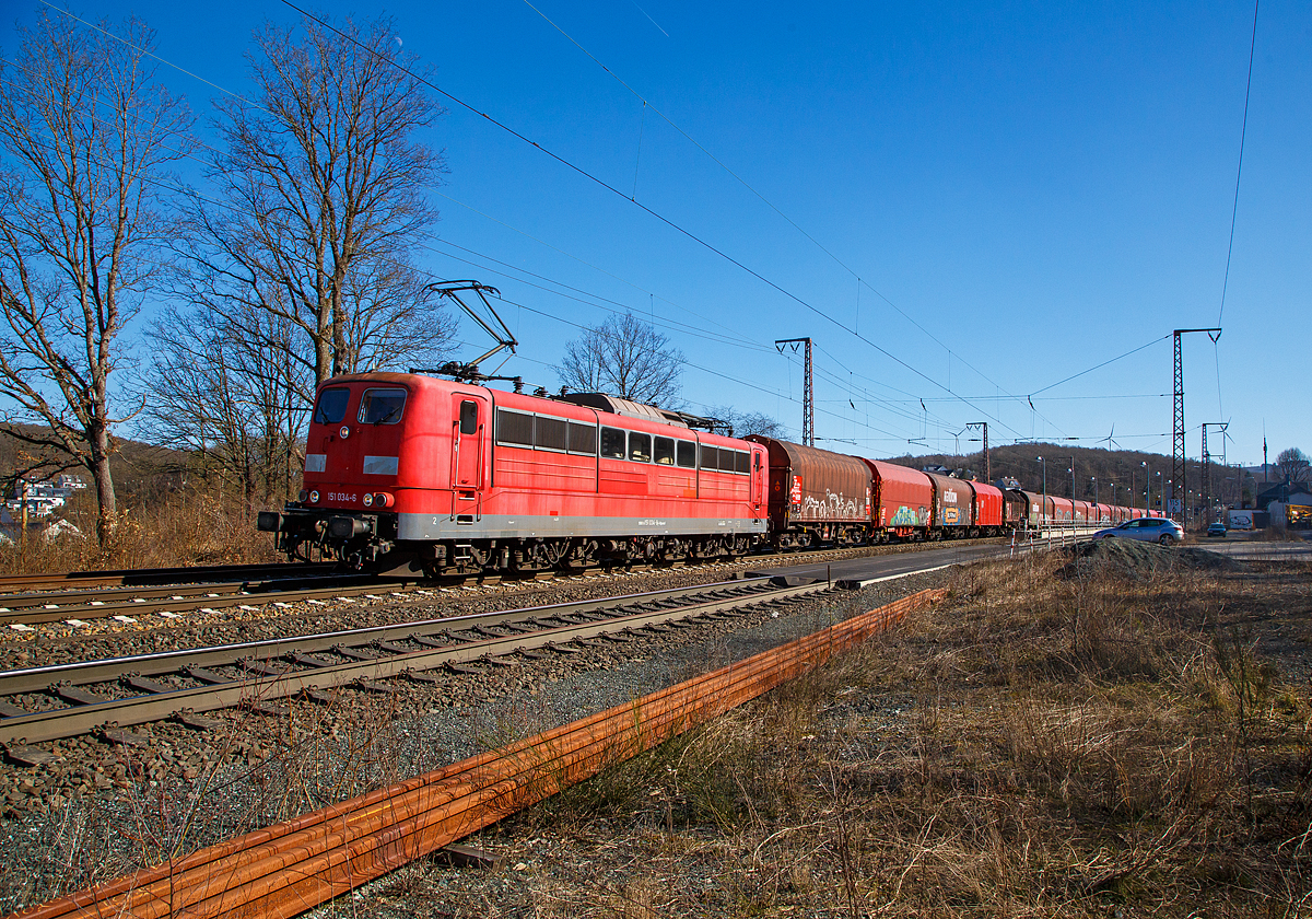 Die an die DB Cargo AG vermietete Railpool 151 034-6 (91 80 6151 034-6 D-Rpool) fährt am 10.03.2022 mit einem Coilzug durch Wilnsdorf-Rudersdorf in Richtung Kreuztal. Diese sechsachsigen Loks (Co’Co’) sind immer noch starke Zugpferde, und so manche moderne Lok hat nicht diese Leistungsfähigkeit.

Die Lok wurde 1974 von der Krauss-Maffei AG in München-Allach unter der Fabriknummer 19653 gebaut und an die Deutsche Bundesbahn geliefert. Bis zum 31.12.2016 gehörte sie zur DB Cargo AG. Zum 01.01.2017 wurden je 100 sechsachsige elektrische Altbau-Lokomotiven der Baureihen 151 und 155 an ein Konsortium aus dem Lokvermieter Railpool verkauft. Die DB Cargo mietet daraufhin 100 Loks von Railpool wieder an. Die anderen Maschinen werden dem freien Markt angeboten. 
