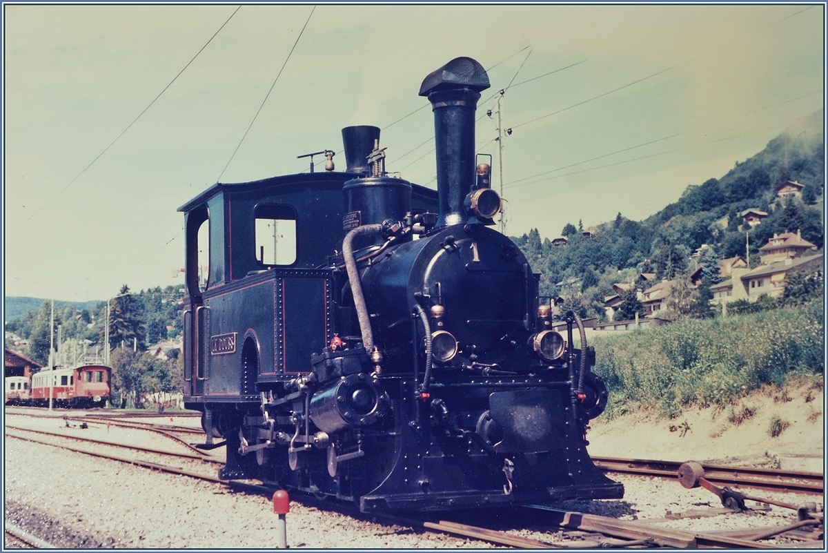 Die kleine, 5,1 Meter lange Dampflok G 3/3 N° 1  Le Doubs  rangiert in Blonay.

Sie wurde 1890 unter der Fabriknummer 618 von der SLM gebaut, und mit zwei weiteren an die  R-d-B (Régional des Brents) geliefert, wo sie bis zur Elektrifizierung der Strecke Le Locle - Les Brents 1950 ihren Dienst versah. In der Folge wurde die Lok der SBB übergeben, mit dem Zweck, sie dem Verkehrshaus der Schweiz in Luzern weiter zu reichen, wobei dann die Lok ab 1973 Leihweise zur Blonay-Chamby Bahn kam. Ab 1976 ging sie in den Besitz der B-C über. Interessanterweise scheinen auch die beiden anderen Lok G 3/3 N°2  Le Père Frédéric und die G 3/3 N° 3  Les Brenets  der Nachwelt erhalten geblieben zu sein. 

Die Lok wurde als leichte Strassenbahnlok mit nur 15 - 16 Tonnen Dienstgewicht gebaut. Die Zylinder arbeiteten zur Vermeidung zu grosser Seitenausladung direkt auf die entsprechend ausgebildete Kuppelstange. Weitere Loks wurden (z.T auch von Krauss&Co München) an folgende Bahnen geliefert: WB (Waldenburgerbahn), FW (Frauenfeld- Wilbahn) und P-S-C (Pont Sage La Chaux de Fondsbahn). (Quelle der Dampfbetrieb der Schweizer Eisenbahnen 1847 - 1966) von Alfred Moser)

Die Analogaufnahme stammt vom August 1985