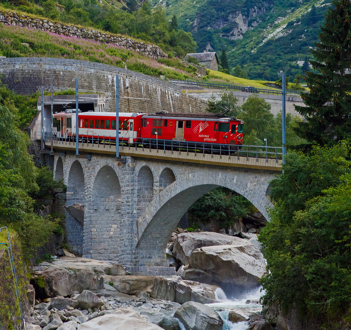 Die MGB Deh 4/4 – 55 „Brig“ schiebt am 01.08.2019 den Sch�llenenbahnzug von G�schenen  nach Andermatt nach hinauf und �berquert hier gerade die Reuss. 

Die Strecke G�schenen–Andermatt ist die Sch�llenenbahn, eine einspurige Zahnradbahn (Zahnstangensystem Abt) im Schweizer Kanton Uri. Sie durchquert die Sch�llenenschlucht der Reuss und weist eine Maximalsteigung von 179 Promille auf, die steilste im MGB-Netz. Die Bahnstrecke wurde zwischen 1913 und 1917 durch die Sch�llenenbahn AG (SchB) gebaut. Die Sch�llenenbahn AG fusionierte 1961 mit der Furka-Oberalp-Bahn (FO), welche wiederum  zum 1. Januar 2003 mit der Zermatt-Bahn (BVZ), zur heutigen Matterhorn-Gotthard-Bahn (MG) fusionierte. 

Heute bef�rdert die Sch�llenenbahn im Jahr ca. 400.000 Reisende. Sie hatte in der Vergangenheit auch eine gro�e milit�rische Bedeutung. Sie versorgte die Festungsanlagen des R�duit im Gotthardmassiv. Die Bahnstrecke hat eine Gesamtl�nge von 3.770 Metern, davon sind 2.509 mit Zahnstange ausger�stet. 1.022 Meter der Strecke befinden sich in Tunneln und 1.110 Meter in Galerien. Die Bahn f�hrt durch f�nf Tunnel und f�nf sch�tzende Galerien. Vier Mal f�hrt die meterspurige Schmalspurbahn �ber eine Br�cke.

Auf der Sch�llenenbahn wurden urspr�nglich vier zweiachsige Elektrolokomotiven f�r kombinierten Adh�sions- und Zahnradbetrieb von SLM und BBC mit Bezeichnung SchB HGe 2/2 eingesetzt. Urspr�nglich liefen sie mit 1.200 Volt Gleichstrom. 1941 wurden sie auf 11.000 Volt Wechselstrom umgestellt. Die letzte dieser vier Lokomotiven wurde 1985 Sp�ter kamen kamen FO BCFhe 2/4 der Schweizerischen Lokomotiv- und Maschinenfabrik mit einem Antrieb der BBC zum Einsatz. ausrangiert. Heute (2019) befahren Deh 4/4 und Wagen der Matterhorn-Gotthard-Bahn die Strecke. Dabei befindet sich das Triebfahrzeug stets am talseitigen Ende, am Zugschluss l�uft ein Steuerwagen.

Die Sch�llenenbahn bietet einen st�ndlichen Pendelverkehr an und ist in den Fahrplan der SBB und der Matterhorn-Gotthard-Bahn vollst�ndig integriert.