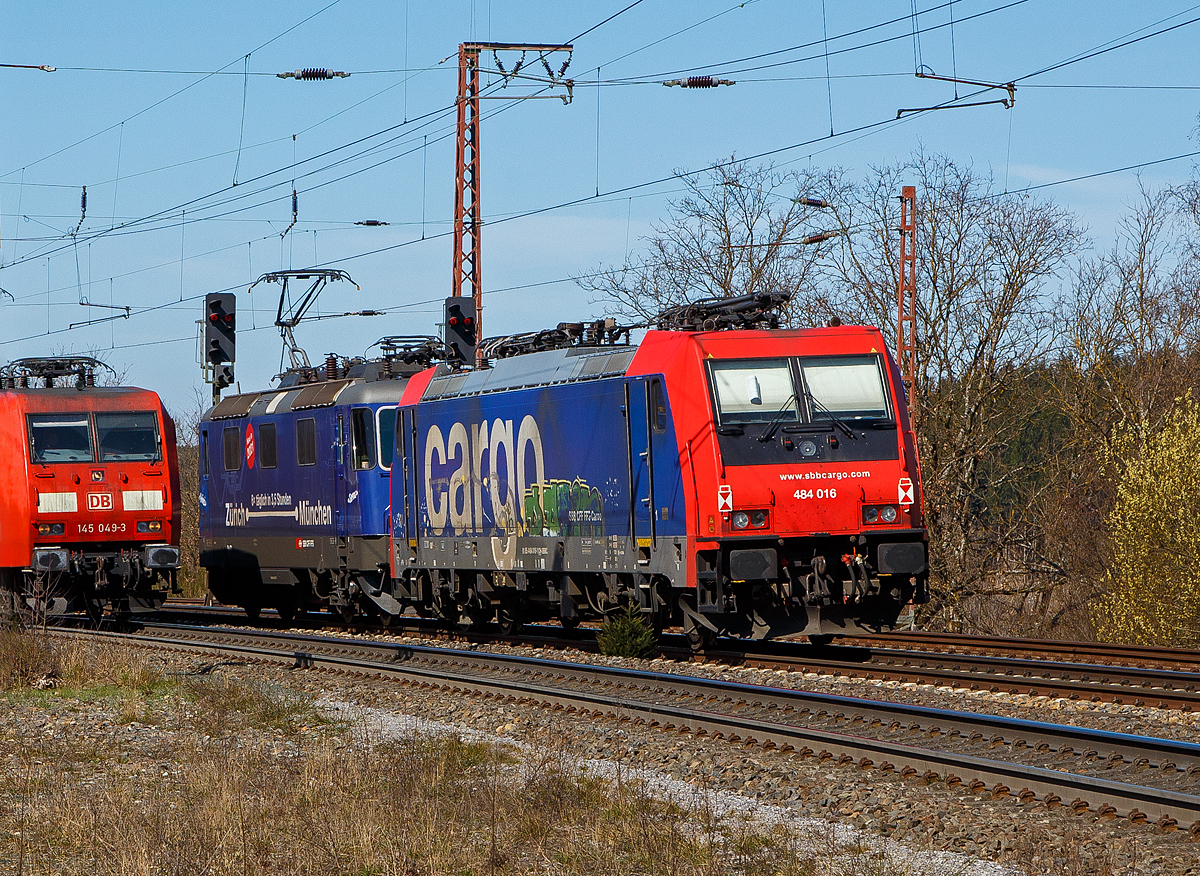 Die SBB Cargo Re 484 016-1(91 85 4484 016-1 CH-SBBC), ex E 484.016 SR, eine TRAXX F140 MS, geschleppt am Haken der SBB Cargo Re 421 371-6 (91 85 4421 371-6 CH-SBBC), ex Re 4/4 II 11371, mit Werbung Zürich – München 6 x täglich in 3,5 Stunden, haben am 30.03.2021 in Rudersdorf (Kr. Siegen) Hp 0, bevor es in Richtung Siegen weitergeht. Links kommt gerade in Gegenrichtung die DB 145 049-3 mit einem Containerzug. Eigentlich ist komplette Dillstrecke (KBS 445) zweigleisig, aber hier ist wohl ein Gleis gesperrt. 

Eine SBB Cargo Re 484 wie die 016-1 kann man eigentlich Deutschland nur mit viel Glück sehen, denn sie haben nur die Zulassungen für die Schweiz und Italien. Sie haben keinen Stromabnehmer mit breiterer Wippe gemäß deutscher Vorschrift, auch die die deutsche Zugsicherung Indusi fehlt ihnen. Der Lz war auf dem Weg nach Krefeld.

Lebensläufe:
Die Re 421 371-6 wurde 1983 von der SLM Winterthur (Elektrik BBC/ SAAS) unter der Fabriknummer 5235 gebaut und als Re 4/4 II 11371 an die SBB geliefert. Im Jahr 2002 erfolgte der Umbau zur Re 421 für die SBB Cargo (Einsatz auch in Deutschland). Die zugelassene Höchstgeschwindigkeit für die Schweiz beträgt 140 km/h und für Deutschland 120 km/h.

Die Re 484 016-1 eine Bombardier TRAXX F140 MS wurde 2004 von Bombardier in Kassel unter der Fabriknummer 34009 gebaut und an die SBB Cargo AG, als E 484.016 SR geliefert.


