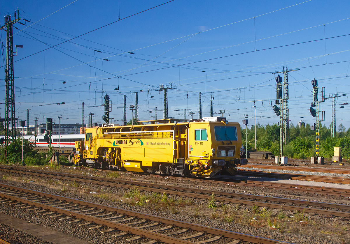 
Die Universal-Stopfmaschine Unimat-Sprinter ESM 865 der DB Netz AG (Schweres Nebenfahrzeug Nr.  97 43 52 004 17-6) ist am 01.06.2017 bein Bahnhof Hamm (Westf.) abgestellt (Bild aus einem Zug heraus).

Die Stopfmaschine (ESM – 08 – 275 / Sprinter) wurde 2000 von Plasser & Theurer unter der Fabriknummer 1164 gebaut und an die DB Netz AG geliefert..

Die 08-275 UNIMAT-Sprinter sind eine speziell für die Einzelfehlerbehebung entwickelte Stopfmaschine. Sie ist mit zwei Weichenstopfaggregaten mit jeweils vier Schwenkpickeln zur universellen Bearbeitung von Strecken und Weichen ausgestattet. Das kombinierte Hebe- und Richtaggregat besteht aus einem Hebehaken, einer Richtrolle und einer Rollhebezange pro Schienenstrang. Für eine schnelle Überstellung zur Baustelle ist die Maschine mit einem hydrodynamischen Antrieb für eine Höchstgeschwindigkeit von 100 km/h ausgelegt. Flankenpflüge, die im Bereich des vorderen Drehgestells montiert sind und eine Kehrbürste am hinteren Ende der Maschine, sorgen nach den Stopfarbeiten für die Herstellung des geforderten Schotterprofils. So ist sie eigentlich eine Stopfmaschine und Schotterpfug.

