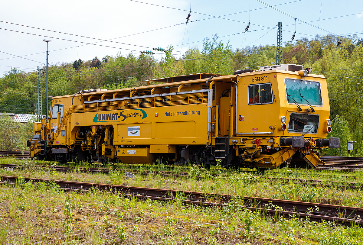 
Die Universal-Stopfmaschine Unimat-Sprinter ESM 866 der DB Netz AG (Schweres Nebenfahrzeug Nr. 97 43 52 006 17-1) steht am 14.05.2017 im Betzdorf/Sieg im Abstellbereich. 

Die Stopfmaschine (ESM – 08 – 275 / Sprinter) wurde 2000 von Plasser & Theurer unter der Fabriknummer 1169 gebaut und an die DB Netz AG geliefert.

Der Unimat-Sprinter ist eine von Plasser und Theurer entwickelte Stopfmaschine für Gleise, Weichen und Kreuzungen, speziell konzipiert für die rasche und präzise Behebung von Einzelfehlern. Daher auch die Abkürzung ESM = EinzelfehlerStopfMaschine.

Die typische Länge eines Einzelfehlers beträgt 9 bis15 Schwellen, er kann sich in Einzelfällen aber bis zu 100 m weit erstrecken. Die Ursachen liegen nicht im direkten Zusammenhang mit Nivellier- und Richtarbeiten oder Zugbelastungen, sondern vielmehr in punktuellen, scharf abgegrenzten Schwächen im Unterbau, Frostschäden usw.. Da dieser Einzelfehler in einem völlig intakten Abschnitt liegt, der keiner durchgehenden Behandlung bedarf, ist es viel zu aufwendig, solche Abschnitte zur Gänze zu bearbeiten. Die Behebung eines Einzelfehlers ist aber unumgänglich, da nicht nur Gründe wie kostspielige Langsamfahrstellen dafür sprechen, sondern auch die Sicherheit des Fahrweges garantiert werden muss.

Die Besonderheit des Einzelfehlers ist, dass er in einem Gleisabschnitt liegt, der ansonsten innerhalb der Toleranzen liegt. Nicht die Solllage  des Gleises ist der geforderte Standard, sondern der  tatsächliche,  durchschnittliche Gleislagefehler muß herangezogen werden. Dafür ist es erforderlich, beide Schienenstränge getrennt auf zumessen, auszuwerten und individuell anzupassen. Für die spezielle Aufgabe der Einzelfehlerbehebung wurde eine neue Software für den Automatischen  Leitcomputer  ALC  entwickelt.  Um die Längshöhe jedes Stranges im Bereich des Einzelfehlers übergangslos an die Qualität des vorangegangenen bzw. nachfolgenden Abschnittes anzupassen, erfolgt deren Korrektur für beide Schienenstränge getrennt.

Der UNIMAT SPRINTER ist eine speziell für die Einzelfehlerbehebung entwickelte Stopfmaschine. Sie ist mit zwei Weichenstopfaggregaten mit jeweils vier Schwenkpickeln zur universellen Bearbeitung von Strecken und Weichen ausgestattet. Das kombinierte Hebe- und Richtaggregat besteht aus einem Hebehaken, einer Richtrolle und einer Rollhebezange pro Schienenstrang. Für eine schnelle Überstellung zur Baustelle ist die Maschine mit einem hydrodynamischen Antrieb für eine Höchstgeschwindigkeit von 100 km/h ausgelegt. Flankenpflüge, die im Bereich des vorderen Drehgestells montiert sind und eine Kehrbürste am hinteren Ende der Maschine, sorgen nach den Stopfarbeiten für die Herstellung des geforderten Schotterprofils.

Die Arbeitsweise mit dieser Maschine ist wie folgt:
- Fahrt zur Baustelle mit einer Höchstgeschwindigkeit von 100 km/h.
- Aufmessen der aktuellen Gleislage mit Hilfe der maschineneigenen  Messsysteme.
- Optimierung der Einzelfehlerbehebung mit dem Programm Win-ALC Sprinter.
- Heben, Richten und Stopfen des ausgewählten Gleisabschnittes.
- Nachmessen des gestopften Bereichs.
- Digitale Aufzeichnung und Archivierung bzw. bei Bedarf Ausdruck   der Daten zwecks Dokumentation.
- Freigabe der Strecke.

Technische Daten der UNIMAT SPRINTER:
Spurweite: 1.435 mm
Achsanzahl: 4 (in 2 Drehgestellen)
Länge über Puffer: 18.140 mm
Drehzapfenabstand: 10.500 mm
Achsabstand im Drehgestell: 1.500 mm
Raddurchmesser: 730 mm (neu)
Eigengewicht: 54t
Anhängelast: 40 t
Höchstgeschwindigkeit: 100 km/h
Zugelassen zur Mitfahrt: 4 Pers.
Kleinster befahrbarer Kurvenradius: R 90 m
Zugelassen für Streckenklasse: A und höher