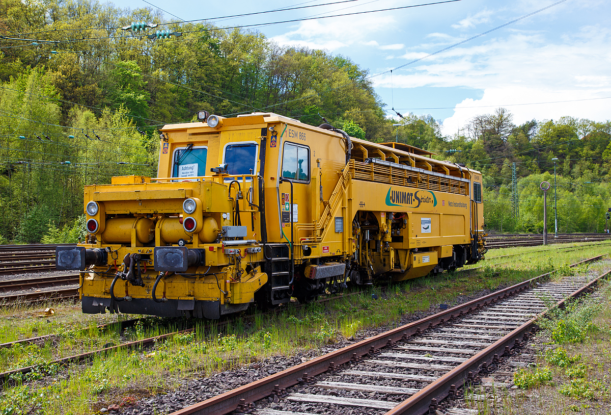 
Die Universal-Stopfmaschine Unimat-Sprinter ESM 866 der DB Netz AG (Schweres Nebenfahrzeug Nr. 97 43 52 006 17-1) steht am 14.05.2017 im Betzdorf/Sieg im Abstellbereich. 

Die Stopfmaschine (ESM – 08 – 275 / Sprinter) wurde 2000 von Plasser & Theurer unter der Fabriknummer 1169 gebaut und an die DB Netz AG geliefert.

Der Unimat-Sprinter ist eine von Plasser und Theurer entwickelte Stopfmaschine für Gleise, Weichen und Kreuzungen, speziell konzipiert für die rasche und präzise Behebung von Einzelfehlern. Daher auch die Abkürzung ESM = EinzelfehlerStopfMaschine.

Die typische Länge eines Einzelfehlers beträgt 9 bis15 Schwellen, er kann sich in Einzelfällen aber bis zu 100 m weit erstrecken. Die Ursachen liegen nicht im direkten Zusammenhang mit Nivellier- und Richtarbeiten oder Zugbelastungen, sondern vielmehr in punktuellen, scharf abgegrenzten Schwächen im Unterbau, Frostschäden usw.. Da dieser Einzelfehler in einem völlig intakten Abschnitt liegt, der keiner durchgehenden Behandlung bedarf, ist es viel zu aufwendig, solche Abschnitte zur Gänze zu bearbeiten. Die Behebung eines Einzelfehlers ist aber unumgänglich, da nicht nur Gründe wie kostspielige Langsamfahrstellen dafür sprechen, sondern auch die Sicherheit des Fahrweges garantiert werden muss.

Die Besonderheit des Einzelfehlers ist, dass er in einem Gleisabschnitt liegt, der ansonsten innerhalb der Toleranzen liegt. Nicht die Solllage  des Gleises ist der geforderte Standard, sondern der  tatsächliche,  durchschnittliche Gleislagefehler muss herangezogen werden. Dafür ist es erforderlich, beide Schienenstränge getrennt auf zumessen, auszuwerten und individuell anzupassen. Für die spezielle Aufgabe der Einzelfehlerbehebung wurde eine neue Software für den Automatischen  Leitcomputer  ALC  entwickelt.  Um die Längshöhe jedes Stranges im Bereich des Einzelfehlers übergangslos an die Qualität des vorangegangenen bzw. nachfolgenden Abschnittes anzupassen, erfolgt deren Korrektur für beide Schienenstränge getrennt.

Der UNIMAT SPRINTER ist eine speziell für die Einzelfehlerbehebung entwickelte Stopfmaschine. Sie ist mit zwei Weichenstopfaggregaten mit jeweils vier Schwenkpickeln zur universellen Bearbeitung von Strecken und Weichen ausgestattet. Das kombinierte Hebe- und Richtaggregat besteht aus einem Hebehaken, einer Richtrolle und einer Rollhebezange pro Schienenstrang. Für eine schnelle Überstellung zur Baustelle ist die Maschine mit einem hydrodynamischen Antrieb für eine Höchstgeschwindigkeit von 100 km/h ausgelegt. Flankenpflüge, die im Bereich des vorderen Drehgestells montiert sind und eine Kehrbürste am hinteren Ende der Maschine, sorgen nach den Stopfarbeiten für die Herstellung des geforderten Schotterprofils.

Die Arbeitsweise mit dieser Maschine ist wie folgt:
- Fahrt zur Baustelle mit einer Höchstgeschwindigkeit von 100 km/h.
- Aufmessen der aktuellen Gleislage mit Hilfe der maschineneigenen  Messsysteme.
- Optimierung der Einzelfehlerbehebung mit dem Programm Win-ALC Sprinter.
- Heben, Richten und Stopfen des ausgewählten Gleisabschnittes.
- Nachmessen des gestopften Bereichs.
- Digitale Aufzeichnung und Archivierung bzw. bei Bedarf Ausdruck   der Daten zwecks Dokumentation.
- Freigabe der Strecke.

Technische Daten der UNIMAT SPRINTER:
Spurweite: 1.435 mm
Achsanzahl: 4 (in 2 Drehgestellen)
Länge über Puffer: 18.140 mm
Drehzapfenabstand: 10.500 mm
Achsabstand im Drehgestell: 1.500 mm
Raddurchmesser: 730 mm (neu)
Eigengewicht: 54t
Anhängelast: 40 t
Höchstgeschwindigkeit: 100 km/h
Zugelassen zur Mitfahrt: 4 Pers.
Kleinster befahrbarer Kurvenradius: R 90 m
Zugelassen für Streckenklasse: A und höher