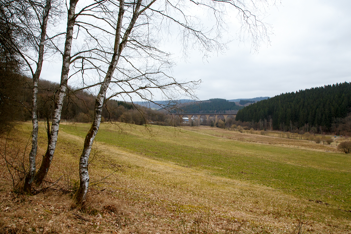 
Ein anderer Blick auf den Rudersdorfer Viadukt am 19.03.2016. 

Der Rudersdorfer Viadukt ist eines der drei Ingenieur-Großbauwerke im nördlichen Abschnitt der Dillstrecke (KBS 445) zwischen Siegen und Haiger auf dem Gebiet des heutigen Ortsteils Rudersdorf der Gemeinde Wilnsdorf, im Bereich von Streckenkilometer 114,9. Aufgrund der schwierigen Topografie und der begrenzten technischen Möglichkeiten war eine direkte Verbindung zwischen Siegen, Haiger und darüber hinaus Dillenburg zum Zeitpunkt des Baus der Deutz-Gießener Bahn vom heutigen Köln-Deutz nach Gießen beim Bau dieser Strecke in den 1850er-Jahren noch nicht möglich. Erst 1915 wurde diese direkte Verbindung zwischen Siegen und Haiger fertiggestellt. Das war vor allem für den aus dem Ruhrgebiet nach Süden führenden Kohleverkehr wichtig. Möglich wurde diese Streckenführung durch die drei großen Ingenieurbauwerke: Den Niederdielfener Viadukt, den Rudersdorfer Viadukt und den Rudersdorfer Tunnel. 

Bei diesem trüben Wetter war mit dieser Blende so kein Bild mit Zug möglich, so muss ich wohl an diese etwas höhere Fotostelle noch mal bei besserem Licht hin...
