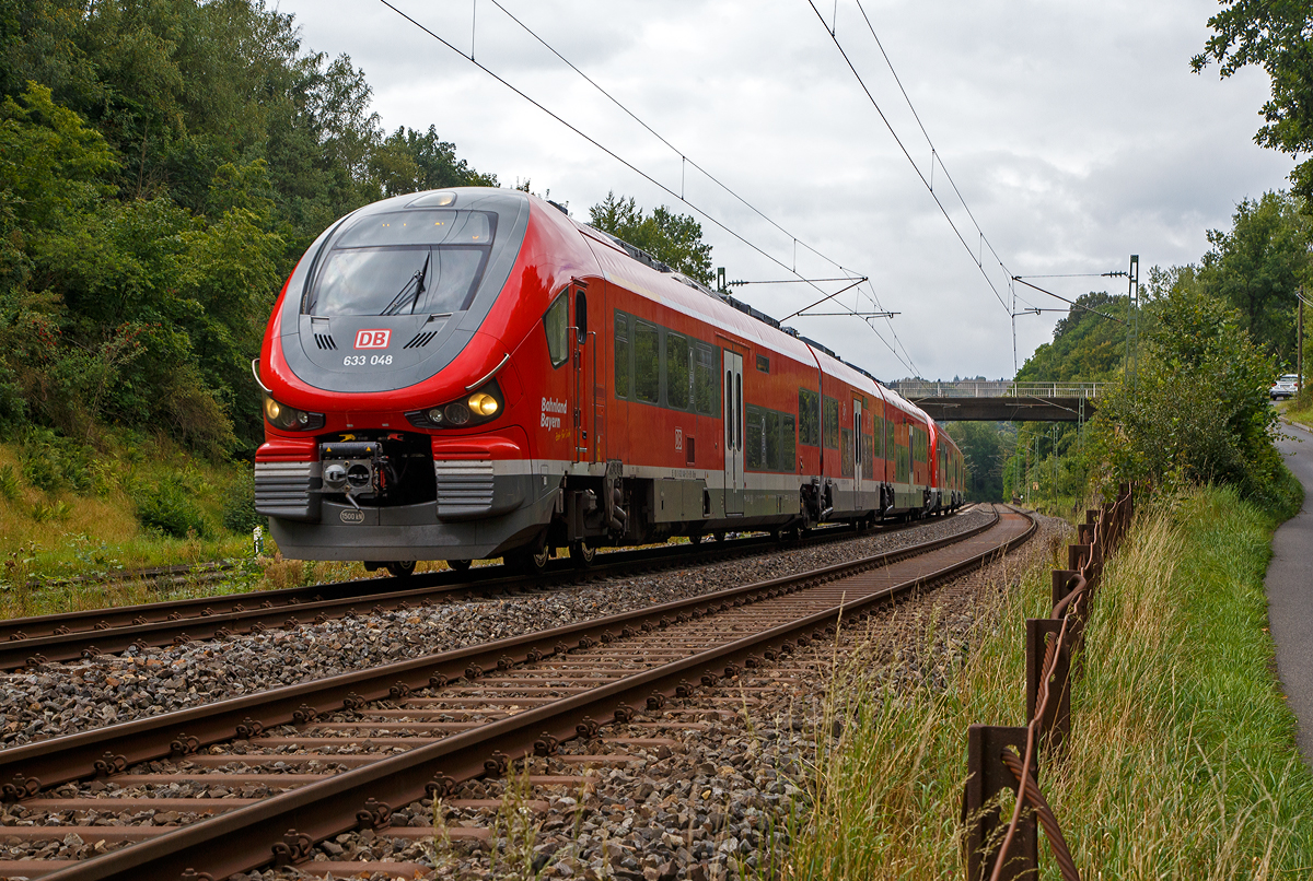 Vermutlich auf einer Überführungsfahrt, wobei der Zugzielanzeiger Kraków Główny (Krakau Hauptbahnhof) zeigt, was ich nicht ganz glaube....
Zweigekuppelte dreiteilige PESA LINK III – 633 048 / 933 048 / 633 548 und 633 542 / 933 042 / 633 042 der DB Regio Bayern fahren am 26.08.2021 bei Wissen (Sieg) über die Siegstrecke (KBS 460) in Richtung Siegen.

Die PESA LINK III wurden 2019 von PESA - Pojazdy Szynowe PESA Bydgoszcz SA in Bydgoszcz (deutsch Bromberg) gebaut,
vorne der 633 048 ff unter der Fabriknummer A643BNA085 und der hintere 633 042 ff unter der Fabriknummer A643BNA079.

Eigentlich war für Dezember 2017 schon der Einsatz im Dieselnetz Allgäu geplant, aber die Triebzüge passten nicht ins deutsche Lichtraumprofil, sie waren wenige Millimeter zu breit  und so gab es keine Zulassung. Der polnische Hersteller PESA musste die Züge umkonstruieren. Danach gab es weitere Probleme, die Fahrzeuge entsprachen nicht den bestellten technischen Anforderungen hinsichtlich des Gewichtes und des Antriebes, so musste PESA erneut eine Umkonstruktion an dem Fahrzeugmodell vornehmen. Am 30. Mai 2018 hat das Eisenbahnbundesamt EBA die Zulassung für den Einsatz der zweiteiligen Züge vom Typ Pesa Link II (BR 632) für die DB Regio nun erteilt. Für die dreiteiligen Pesa Link III (BR 633) wurde sie mittlerweile auch erteilt. 

Warum es aber solange braucht um Normen und Lastenhefte zu lesen entzieht sich meiner Kenntnis. 

Der PESA LINK (Projektname DMU 120) ist ein Dieseltriebwagen des polnischen Herstellers PESA (Pojazdy Szynowe Pesa Bydgoszcz SA). Die ČD (Tschechische Bahnen) vermarkten sie als „RegioShark“ (RegioHai). Hai war auch mein erster Eindruck, im September 2014 auf der InnoTrans 2014 in Berlin, als das erste Vorserienfahrzeug 631 001-4 vorgestellt wurde.

Es werden verschiedene Varianten von ein- bis vierteiligen Triebzügen, mit unterschiedlichen Motorleitungen, angeboten.

Der Innenraum des Pesa Link ist im Mittelteil in Niederflurbauweise ausgeführt, während die Fahrgastbereiche an den Fahrzeugenden hochflurig ausgelegt sind. Die Bodenhöhe des Niederflurbereichs beträgt in der DB-Version im 600 mm. Je ein Motor treibt jeweils beide Achsen eines Drehgestells (Enddrehgestell) am Fahrzeugende an. Zwischen den Endwagenteilen und dem mittleren Wagenteil befinden sich jeweils nicht angetriebene Jakobsdrehgestelle. 

Der Antrieb erfolgt diesel-hydromechanisch durch 2 Stück MTU 12 Zylinder, 4-Takt Dieselmotor (PowerPack) mit Abgasturbolader und Ladeluftkühlung vom Typ 12V 1600 R70LP mit einer Leistung von 625 kW, über ein 6-Gang-Automatik-Getriebe ZF EcoLife Rail (480 kW), jeweils auf die beide Achsen eines Enddrehgestelles

Technische Daten der BR 633 (DB):
Spurweite: 1.435 mm (Normalspur)
Achsformel: B’(2’)(2’)B’
Länge über Puffer:  57.130 mm
Höhe: 4.206 mm
Breite: 2.800 mm
Drehzapfenabstand: 17.040 mm
Achsabstand im Drehgestell: 2.100 mm
Dienstgewicht: 120,4 t
Achslast: 18,9 t
Höchstgeschwindigkeit: 140 km/h
Installierte Leistung: 2 x 625 kW (2 x 838 PS)
Beschleunigung:  0,74 m/s²  bei 0-30 km/h
Antrieb: MTU Powerpack 12 Zylinder, 4-Takt-Dieselmotor mit Abgasturbolader und Ladeluftkühlung vom Typ MTU 6H 1800 R85L
Motornenndrehzahl: 2.100 U/min
Motorhubraum: 21  l
Getriebe: 6-Gang-ZF-Automatikgetriebe EcoLife Rail (480 kW),
Kraftübertragung: diesel-hydromech.  
Fußbodenhöhe (Niederflurber.):   600 mm                              
Fußbodenhöhe (Hochflurber.):   1.290 mm
Kleinster bef. Halbmesser: 100 m (Werkstatt) / 150 m (Betrieb)
Kupplungstyp:  Scharfenberg Typ 10
Sitzplätze in der 1. Klasse: 12
Sitzplätze in der 2. Klasse: 94 und 54 Klappsitze
Fahrradstellplätze: 36 (dann keine klappsitze)
Stehplätze: 196