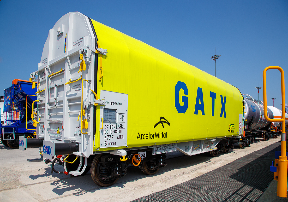 Vierachsiger Drehgestell-Flachwagen mit verschiebbarem Planenverdeck und Lademulden f�r Coiltransporte, 31 80 4777 483-8 D-GATED, der Gattung Shimmns-ttu, der GATX wurde auf der Messe “transport logistic 2019“ in M�nchen (hier 05.06.2019) pr�sentiert.

ArcelorMittal bestellte bei GATX 60 dieser Shimmns-ttu-Wagen f�r seine europ�ischen Verkehre. Gebaut wurden die Wagen vom kroatischen Wagenbauer �uro �akovic.

Diese Wagen sind speziell f�r den Transport witterungsempfindlicher Blechrollen (Coils) bestimmt. Er besitzt feste Stirnw�nde, 5 fest im Untergestell eingebaute Lademulden. Die Wagenabdeckung erfolgt mit einer PVC-beschichteten Gewebeplane, die auf 11 Rohrrahmen aufliegt. �ber Laufwagen ist das Planendach in Wagenl�ngsrichtung verschiebbar. Die Verriegelung des Planendaches an den Stirnw�nden erfolgt �ber eine 4-Punkt-Zentralverriegelung, die sowohl vom Erdboden als auch von der Rampe aus bedient werden kann. Das Planenverdeck l�sst sich an einem Wagenende so weit zusammenschieben, dass ca. 2/3 der Ladefl�che zur Beladung freigegeben wird.Hierdurch ist eine einfache Beladung des Wagens sowohl von oben als auch von der Seite aus m�glich. 

TECHNISCHE DATEN:
Spurweite: 1.435 mm
Achsanzahl: 4 (in 2 Drehgestelle)
L�nge �ber Puffer: 12.040 mm
L�nge der Ladefl�che: 10.800 mm
Drehzapfenabstand: 7.000 mm
Achsabstand im Drehgestell: 1.800 mm
Eigengewicht:  21.800 kg
H�chstgeschwindigkeit: 100  km/h (beladen) / 120 km/h (leer)
Maximales Ladegewicht: 68,2 t (Streckenklasse D4)
Kleinster bef. Gleisbogenradius: 35 m
Bauart der Bremse: KE-GP-A
Intern. Verwendungsf�higkeit: TEN
