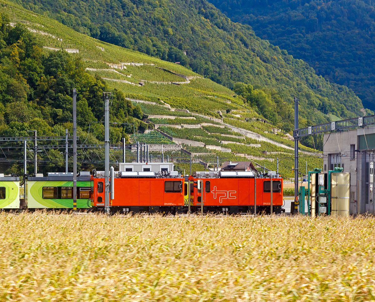 
Vor dem Depot der TPC (Transports Publics du Chablais SA) in Aigle stehen am 16.09.2017 die beiden Zweikraft Diesel-Zahnrad-/Adhäsionslokomotiven HGem 2/2 943 und HGem 2/2 941.

Die 5 Schweizer Schmalspurbahnen MOB, MVR, TPC, TPF und NStCM  haben im August 2012 bei Stadler maßgeschneiderte  Zweikraft  Diesel-Zahnrad- und Adhäsionslokomotiven der Typen HGem 2/2 und Gem 2/2  bestellt.  Die Lokomotiven werden den Infrastrukturdivisionen zugeteilt  und für Baueinsätze, Schneeräumung und Interventionsfahrten eingesetzt.  

Dank ihrer Bi-Modalität schlummert in den Loks großes Potenzial: Zur Beförderung von schweren Bauzügen können die Lokomotiven in Vielfachsteuerung eingesetzt werden und umweltschonend elektrisch zur Arbeitsstelle fahren. Für das Manöver vor Ort bei abgeschalteter Fahrleitung oder einer Fahrleitungsstörung ist ein moderner, leistungsfähiger Dieselmotor vorhanden. Für Spezialeinsätze kann die Lok von einer Funkfernsteuerung aus betrieben werden.

Technische Merkmale:
Drehstrom-Asynchron-Antriebstechnik mit ABB-Stromrichter stufenlos regulierbar mit sehr guten, ökonomischen Langsamfahreigenschaften für die Arbeitseinsätze.
Fahrmotoren und Generator von TSA.
Achtzylinder-Dieselmotor von Mercedes-Benz, Euro IIIB und Partikelfilter.
Rekuperation der Bremsenergie im elektrischen Betrieb möglich, Bremswiderstände für die Fahrt im Dieselbetrieb, resp. bei nicht vorhandener Fahrleitung vorhanden.
Möglichst viele Gleichteile wie bei den diversen Personen-Triebwagen für die gleichen Bahngesellschaften (identische Achsantriebe, Traktionselektronik, Leittechnikmodule, Führerstand-Bedienelemente, Druckluftanlagen etc.)
Umfangreiche Beleuchtungsmittel zusätzlich zur Frontbeleuchtung: Suchscheinwerfer, Warnleuchten, Kupplungsausleuchtung, Fahrzeuglängsbeleuchtung.
Bordnetz 400 VAC
Platz für bis zu 10 Personen in der Lok (Bauzüge)

TECHNISCHE DATEN HGem 2/2 der TPC:
Anzahl: 3
Spurweite: 1.000 mm  
Lieferjahre: 2016–2017  
Eigengewicht: 28 t
Länge über Kupplung: 8.370 mm
Länge über Kasten: 7.550 mm               
Achsstand: 4.250 mm 
Fahrzeugbreite: 2.700 mm
Fahrzeughöhe: 3.874 mm
Treibraddurchmesser neu/alt: 876 / 852 mm
Zahnraddurchmesser neu/alt: 798 / 774 mm
max. Leistung am Rad: 700 kW 
max. Leistung im Bremsbetrieb: 700 kW  
max. Leistung im Dieselbetrieb: ca. 400 kW 
Max. Anfahrzugkraft am Rad Adhäsion: 70 kN  
Max. Anfahrzugkraft am Zahnrad: 135 kN
Zuladung:  0.8 t / 8 Sitzplätze
Höchstgeschwindigkeit Adhäsion: 60 km/h
Höchstgeschwindigkeit Zahnrad bergwärts bei 230-135‰ : 25 km/h 
Höchstgeschwindigkeit Zahnrad talwärts bei 230‰ : 13 km/h
Höchstgeschwindigkeit Zahnrad talwärts bei 200‰ : 14 km/h
Höchstgeschwindigkeit Zahnrad talwärts bei 170‰ : 15,5 km/h
Höchstgeschwindigkeit Zahnrad talwärts bei 135‰ : 17,5 km/h
Übersetzungsverhältnisse:  Adhäsion 1:11.22 / Zahnrad 1:8.9
Fahrleitungsspannung: 1.500 und 750 VDC
Tankinhalt: ca. 2 x 250 Liter
Hilfsbetriebe: Batterieladung 24VDC, 8kW / 400VAC-HB-Netz 25 kVA  

Quelle: Stadler Rail
