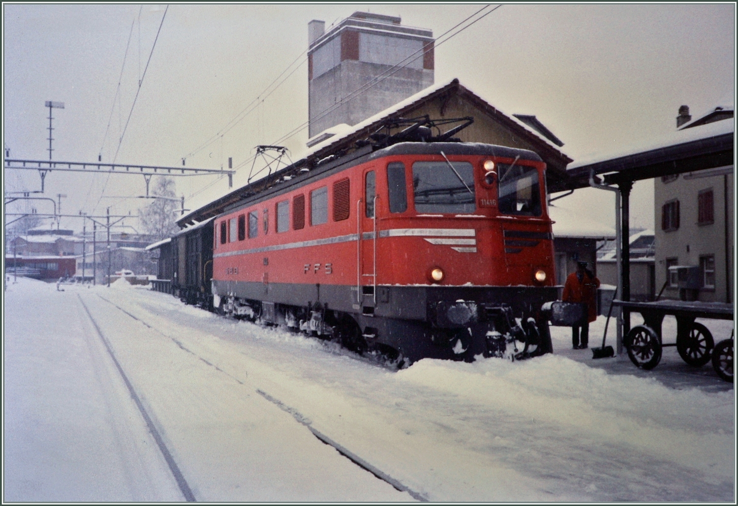An einem trüben und schneereichen Märztag steht die SBB Ae 6/6 11416  Glarus  mit einem Postwagen in Beromünster auf Gleis 1. 

Analogbild vom März 1988