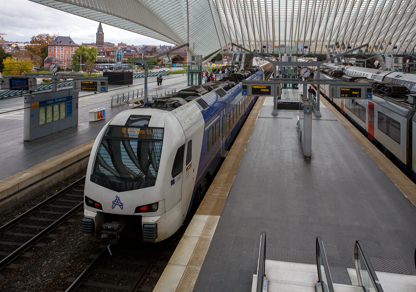 Der dreiteilige, 3-System Stadler FLIRT³ Triebzug 550 (94 84 4 040 550-x NL-AN) der Arriva Personenvervoer Nederland steht am 21 Oktober 2025 im Bahnhof Liège Guillemins (Lüttich-Guillemins), als Dreiländerzug / Drielandentrein / Train des trois pays bzw. RE18 / S 43 (LIMAX - Liège-Maastricht-Aachen-Express (Lüttich über Maastricht nach Aachen) zur Abfahrt bereit. 

Für den Einsatz in der Provinz Limburg beschaffte die Arriva Nederland 38 Triebzüge des Typs Stadler Flirt 3, die ab 2016 in Betrieb gingen. Zum Einsatz kommen dort 15 zwei- und 13 dreiteilige Fahrzeugkompositionen, sowie 8 dieser dreiteiligen Flirt´s in Mehrsystemausstattung (3-System) die von Arriva NL auf dem grenzüberschreitenden Dreiländerzug zwischen Lüttich über Maastricht nach Aachen eingesetzt werden. Die 8 Mehrsystem-FLIRT wurden 2017 bis 2020 in Dienst gesetzt. 

Im Februar 2016 bestellte Arriva Personenvervoer Nederland BV acht dreiteilige FLIRT-Elektrotriebzüge mit Niederflurtechnik bei Stadler. Die Dreisystemzüge können mit 1,5 kV Gleichstrom, 3 kV Gleichstrom und 15 kV Wechselstrom betrieben werden und verkehren im grenzüberschreitenden Regionalverkehr nach Belgien und Deutschland. Die neueste Generation der dreiteiligen FLIRT-Triebzüge ist für eine Höchstgeschwindigkeit von 160 km/h ausgelegt. Sie bieten 172 Sitzplätze, davon 12 in der ersten Klasse und 13 Klappsitze. Die Triebzüge verfügen über Luftfederung und breite Einstiegstüren. Dank des Niederfluranteils von 90 Prozent ist der Zugang zu den klimatisierten Zügen einfach, und die optimale Raumausnutzung gewährleistet ausreichend Platz für Kinderwagen und Rollstühle.

Der Dreiländerzug, niederländisch Drielandentrein, französisch train des trois pays oder LIMAX (Akronym aus Liège-Maastricht-Aachen-Express) ist eine Bahnverbindung, die von Arriva Personenvervoer Nederland betrieben wird.Sie verläuft von Aachen Hbf über Herzogenrath (Deutschland), Heerlen, Maastricht (Niederlande) und Visé nach Liège-Guillemins (Belgien).

Seit dem 29. Januar 2019 verkehren die Züge halbstündlich zwischen Maastricht und Heerlen sowie stündlich grenzüberschreitend bis Aachen. Inzwischen wurde der Halbstundentakt durch den zweigleisigen Ausbau zwischen Heerlen und Landgraaf bis Herzogenrath ausgeweitet. Seit Dezember 2023 wird ebenfalls Aachen zwei Mal pro Stunde erreicht, was vorher durch Trassenkonflikte mit dem RE 4 nicht möglich war. Die stündliche Verlängerung der Linie nach Lüttich fand am 30. Juni 2024 statt. Ziel ist, die Verbindung Lüttich–Maastricht–Aachen im 30-Minuten-Takt zu bedienen.

Der FLIRT (Akronym für Flinker Leichter Innovativer Regionaltriebzug) basiert auf dem Stadler GTW. Der Hauptunterschied besteht darin, dass die Antriebseinheiten des FLIRT hinter den Führerständen angeordnet sind (anstatt in einem separaten Triebwagen). Dieser Zugtyp zeichnet sich durch helle und geräumige Innenräume aus, die durch den Einsatz von Jacobs-Drehgestellen in Kombination mit breiten, offenen Übergängen und einem Niederfluraufbau ermöglicht werden. Der Niederfluraufbau, zusammen mit einer ausziehbaren Trittstufe, verbessert die Zugzugbenutzung für Menschen mit körperlichen Einschränkungen. Das geringe Gewicht des Zuges in Verbindung mit hohem Drehmoment macht ihn ideal für Züge mit häufigen und kurzen Haltezeiten.

Konstruktion:
Die FLIRT-Züge bestehen hier drei Wagen, die an den Wagenübergängen von Jacobs-Drehgestellen getragen werden. Der Einsatz von Jacobs-Drehgestellen ermöglicht kurze und breite Wagenübergänge und sorgt so für hohe Transparenz. Daher verfügen diese Züge über breite Wagenübergänge und einen Niederflureinstieg, wie er bei U-Bahnen und Straßenbahnen üblich ist. Die gute Sicht im gesamten Zug, kombiniert mit den Kameras, soll ein Gefühl der Sicherheit vermitteln. Die Bodenhöhe von 780 mm entspricht der der meisten Bahnsteige. Bis zu drei Züge können im Verbund verkehren.

Im Innenraum gibt es keine Trennwände und Türen; lediglich die erste und zweite Klasse sind durch Glastüren und Trennwände voneinander getrennt. Die Züge sind unter anderem mit Klimaanlage, einem Fahrgastinformationssystem mit TFT-Displays und automatischer Ansage, (Sicherheits-)Kameras und einem Notrufsystem ausgestattet, das nach Betätigung der Notbremse einen akustischen Kontakt zum Lokführer ermöglicht.

Interieur/Innenraum:
Fahrgäste haben Zugang zu USB-Ladestationen für mobile Geräte, Steckdosen und kostenlosem WLAN. Die Züge sind zudem mit einem Niederflurzugang, ausziehbaren Trittstufen und einer rollstuhlgerechten Toilette ausgestattet, um das Reisen für Menschen mit körperlichen Einschränkungen zu erleichtern. Diese Toilette verfügt über eine klappbare Wickelauflage. Die Züge bieten Abteile der ersten und zweiten Klasse, einen Salon und einen Fahrradabstellraum. Die Sitze der ersten Klasse (Kiel Match G2) sind grau mit orangefarbenen Kopfstützen. Die Sitze der zweiten Klasse sind blau-kariert mit dunkelblauen Kopfstützen.

Die 3-System-Züge:
Die Züge sind am neuen Arriva-Logo, den Aufklebern unterhalb der Führerstandsfenster mit dem Text „Kofinanziert von der Europäischen Union“ und den Dreiländerzug-Aufklebern erkennbar. Auf Wunsch Belgiens fehlt an den Führerstands Seiten der, sonst bei Arriva übliche, Limburg-Löwen. Die Züge sind primär für den Schnellzugverkehr konzipiert, sie verfügen über drei Türen pro Seite, viele Sitzplätze, wenige Klappsitze und wenige Fahrrad- oder Rollstuhlplätze. Im internationalen Verkehr werden Reiseinformationen auf Niederländisch, Deutsch und Französisch durchgesagt. Im Mittelteil gibt es zwei querangeordnete Sitzbänke. 

Die 3-System Stadler FLIRT³ (Baureihe IIImcs) erzeugen ein anderes Geräusch als die reine 1,5 kV- Gleichstrom-Triebzüge (Baureihe II und III). Dieses Geräusch wird durch die Traktionsumrichter verursacht, die es dem Triebzug ermöglichen, mit verschiedenen Spannungen zu arbeiten. Diese Umrichter sind von anderer Bauart und nutzen ebenfalls eine Drei-Phasen-Technologie, was ein leichtes Brummen des Triebzugs verursacht. Bei einer Oberleitungsspannung von 1,5 kV unterscheidet sich dieses Geräusch von dem bei 3 kV und 15 kV. Auch bei 1,5 kV ist ein Brummen hörbar, das von einer Drosselspule auf dem Dach stammt.

Technik der 3-System-Züge: 
Die 3-System-Triebzüge verfügen über zwei Stromabnehmer auf dem Mittelwagen, einen für Gleichstrom (1,5 und 3 kV) und einen für Wechselstrom (15 kV). Hinter jedem Führerstand befindet sich ein Stromumrichter (Fabrikat ABB, Type BORDLINE CC1500 MS_15-3-1.5kV_M_1300_070A01), der die Oberleitungsspannung in Drehstrom für die Fahrmotoren umwandelt. Die Umrichter arbeiten mit schnell schaltenden IGBTs; die Schaltfrequenz ist während der Fahrt hörbar. Beide Fahrmotoren (Fabrikat TSA, Type TMF 59-33-4 (600 kW)) eines Drehgestells werden gemeinsam gesteuert. Die Zugkraft der Fahrmotoren wird über ein Zahnradgetriebe mit einem Übersetzungsverhältnis von 1:5,347 auf die Achsen übertragen.

Auslieferung:
Der erste 3-System-Zug (550) wurde am 19. September 2017 über Venlo ausgeliefert. Da ein belgisches Gesetz (von 2014) die Ausstattung neuer Züge im Schienennetz mit dem ETCS-Sicherheitssystem vorschreibt, mussten die IIImcs entsprechend ausgerüstet werden. Dies erfolgte im Zeitraum 2021–2023 bei Stadler Refit in Blerick. Die ersten Testfahrten in Belgien fanden am 1. Juni 2022 statt, die Züge 550 und 555 waren bereits mit ETCS ausgestattet, andere noch nicht. Die endgültige Umrüstung auf ETCS erfolgte 2023, woraufhin Anfang 2024 Testfahrten und die Zulassung für Belgien folgten.

TECHNISCHE DATEN der 3-System Stadler FLIRT³:
Gebaute Anzahl: 8 (dreiteilig)
Nummerierung: 550 bis 557
Hersteller: Stadler Rail
Baujahre: ab 2017
Spurweite: 1.435 mm (Normalspur)
Achsfolge: Bo'2'2'Bo' (8 Achsen, davon 4 angetrieben) 
Länge über Kupplung: 63.200 mm
Fahrzeugbreite: 2.820 mm
Fahrzeughöhe: 4.120 mm
Drehzapfenlabstände: 17.600 mm / 17.500 mm / 17.500 mm / 17.600 mm
Achsabstand im Triebdrehgestell: 2.500 mm
Achsabstand im Laufdrehgestell: 2.700 mm
Treibraddurchmesser: 920 mm (neu)
Laufraddurchmesser: 760 mm (neu) / 690 mm (abgenutzt)
Leergewicht: 121 t
Höchstgeschwindigkeit: 160 km/h (in NL und B planmäßig 140 km/h) / 160 km/h (in D)
Sitzplätze: 12 in 1. Klasse, 147 der 2. Klasse davon 13 Klappsitze
Stehplätze: 161 (4 Personen/m²)
Bodenhöhe: Niederflur 780 mm (90%), Hochflur 1.180 mm
Türbreite: 1.300 mm
Türen je Längsseite: 3
Leistung am Rad: 3.000 kW
Anfahrzugkraft: 200 kN
Anzahl der Traktionsmotoren: 4 TSA Typ TMF 59-33-4 (600 kW)
Übersetzung: 1 : 5,347
Stromsysteme: 1,5 kV DC, 3,0 kV DC (Gleichstrom) und 15 kV 16,7 Hz AC (Wechselstrom)
Beschleunigung bis 54 km/h: 0,95 m/s²
Verzögerung: 1,15 m/s²
Kupplung: Scharfenberg