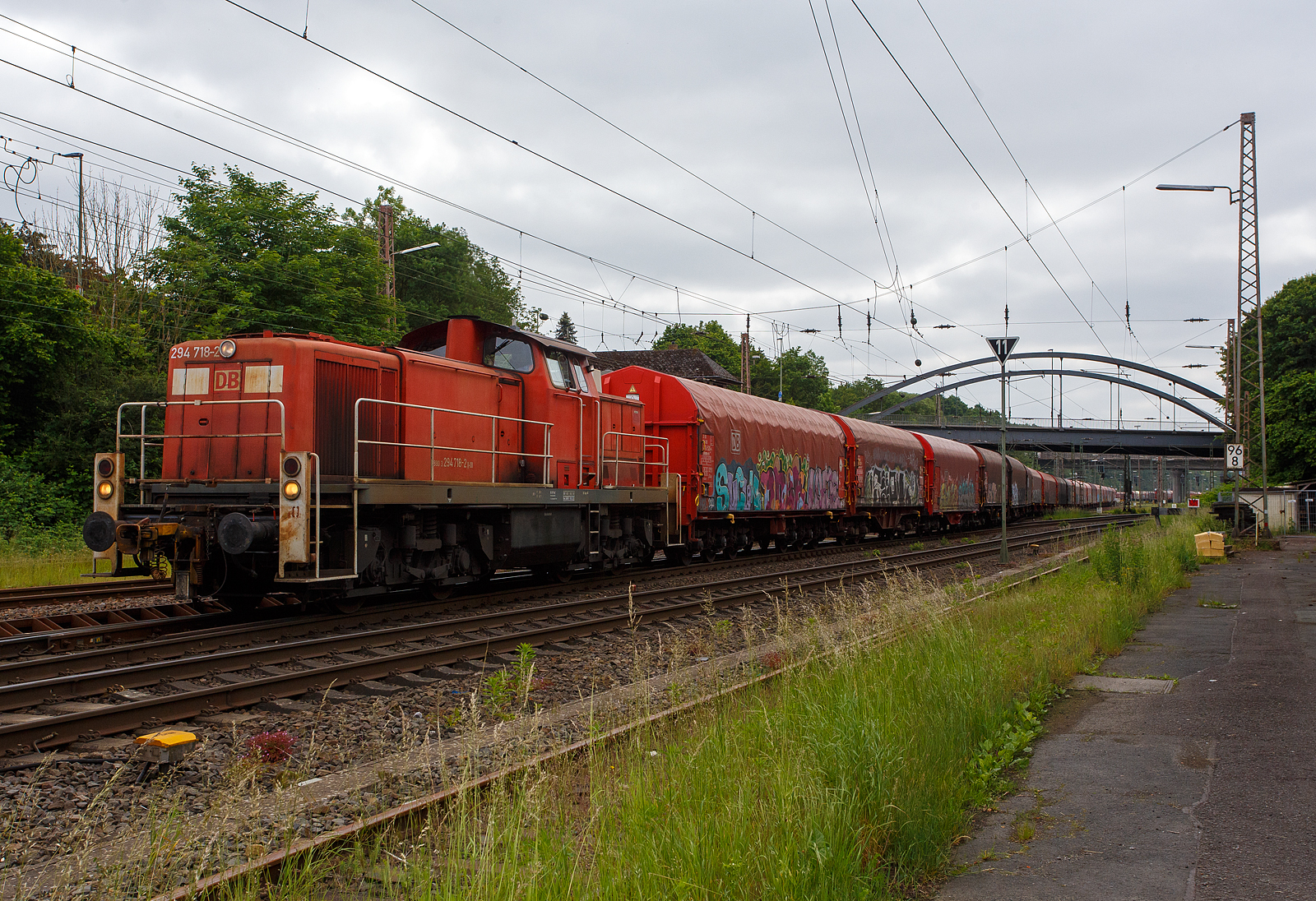 Die 294 718-2 (98 80 3294 718-2 D-DB), eine remotorisierte V 90 der DB Cargo AG drückt am 03 Juni 2024 einen langen Coilzug nun in den Gbf Kreuztal. Der Zug kam vom Werk Kreuztal-Eichen der thyssenkrupp Steel Europe AG (ehem. Eichener Walzwerk).

Die Lok wurde 1971 bei MaK in Kiel unter der Fabriknummer 1000526 gebaut und als 290 218-3 an die DB geliefert. Die Ausrüstung mit Funkfernsteuerung (Typ Krauss-Maffei) und Umzeichnung in 294 218-3 erfolgte 1996. Im Jahr 2002 erfolgte durch die DB Fahrzeuginstandhaltung GmbH, in Cottbus eine Remotorisierung durch einen neuen MTU 90° V-8-Zylinder-Dieselmotor mit Common-Rail-Einspritzsystem, Abgas-Turbolader und Ladeluftkühlung, vom Typ 8V 4000 R41. Der Motor ist auf eine Leistung von 1.000 kW (1.341 PS) bei 1.800 U/min gedrosselt. Auch wurden eine neue Lüfteranlage und ein neuer Luftpresser eingebaut, zudem bekam die Lok ein Umlaufgeländer. Durch die Remotorisierung und den Umbau erfolgte auch die Umzeichnung in die heutige 294 718-2.