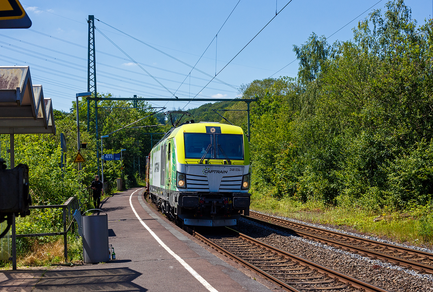 Die an die Dortmunder Eisenbahn GmbH (DE) vermietete SIEMENS Vectron Dual Mode 248 034-1  Phoenix  (90 80 2248 034-1 D-DE) der Captrain Deutschland GmbH fährt am 25 Juni 2024, mit einem Coilzug (Wagen der Gattung Shimmnis-ttu der Ermewa) durch den Bahnhof Scheuerfeld/Sieg in Richtung Siegen. 

Die SIEMENS Vectron DM wurde 2022 von Siemens Mobility GmbH in München-Allach unter der Fabriknummer 23185 gebaut und im Februar 2023 an die Captrain ausgeliefert. Die Lok hat die Zulassung für Deutschland und eine Höchstgeschwindigkeit von 160 km/h. Die Hybridlok (Vectron Dual Mode) kann die Antriebsenergie aus der Fahrleitung beziehen (2.400 kW Leistungen am Rad), oder mittels eines MTU 16V 4000 R84 V16-Zylinder-Dieselmotors (2.400 kW Motorleistung, 2.000 kW Leistungen am Rad) erzeugen. 

Die Dortmunder Eisenbahn GmbH (DE) ist eine private Eisenbahngesellschaft aus Dortmund. Die Dortmunder Eisenbahn GmbH ist ein gemeinsames Tochterunternehmen der Dortmunder Hafen GmbH und der Captrain Deutschland GmbH. Sie ist zu 65 Prozent im Besitz der Captrain Deutschland GmbH (deutsche Tochter der SNCF) und 35 Prozent der Anteile hält die Dortmunder Hafen AG. Die DE Infrastruktur GmbH,  mit ca. 50 Kilometern Gleislänge, gehört zu 81 Prozent der Dortmunder Hafen AG und zu 19 Prozent der Captrain Deutschland GmbH.
