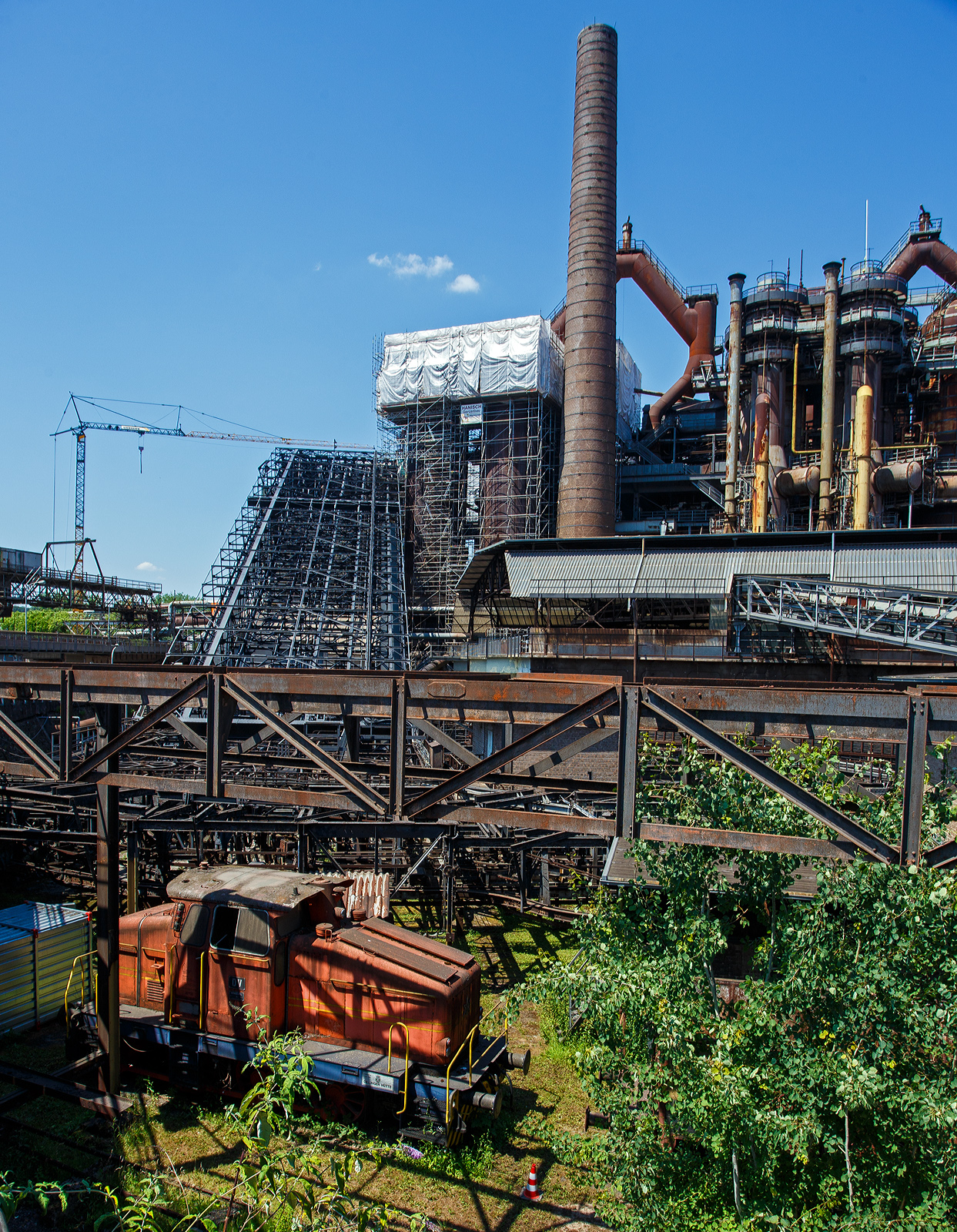 Die ex D V der AG der Dillinger Hüttenwerke (Normalspur – Diesellokomotive 5 /Henschel 29726), eine C-gekuppelte Henschel DH 440 Ca, hier am 01 Juli 2025 als Denkmal ausgestellt im Bereich der Kokssieberei der Völklinger Hütte. 

Die dreifachgekuppelte Lok vom Typ Henschel DH 440 Ca wurde 1959 von der Henschel-Werke GmbH in Kassel unter der Fabriknummer 29726 gebaut und als D V an die AG der Dillinger Hüttenwerke geliefert, wo sie bis 2000 im Dienst war. Die AG der Dillinger Hüttenwerke schenkte 2003 diese Lok dem Weltkulturerbe Völklinger Hütte, heutiger Eigentümer ist die Initiative Völklinger Hütte e.V., diese Lok war nie in Völklingen im Einsatz, aber ähnliche Lokomotiven dieser Bauart werden heute noch im Werksverkehr in Völklingen eingesetzt. Mit solchen Zügen wurden unter anderem Koks zur Kokssieberei transportiert, oder auch Schrottpakete zum Verladen in die Hängebahnwagen. Bei der AG der Dillinger Hüttenwerke sind baugleiche Loks im Werksverkehr in Dillingen im Einsatz. 

Übrigens die AG der Dillinger Hüttenwerke ist heute der einzige Produktionsstandort von Roheisen im Saarland und sie ist das größte Grobblechwerk Europas. Auch wenn die Saarstahl AG mit Anteilseigner ist, so darf man diese gleichsetzen. 

Zu den Loks:
Die Henschel DH 440 Ca sind C-gekuppelte standardisierte Werksbahn-Dieselloks der 3. Generation von Henschel mit dieselhydraulischem Antrieb mittels Kuppelstangen. Die 28 Lok von diesem Typ, mit einem mittelschnell laufenden MAN-Motor, wurden zwischen 1957 und 1965 gebaut. Allein 6 Exemplare wurden an die AG der Dillinger Hüttenwerke geliefert (D V bis D X).

Anders als die DH 440 der 2. Generation hat die DH 440 Ca (der 3. Generation) eine außenliegende Blindwelle (daher auch der Zusatz Ca), es ist auch größte Unterschied. Wobei auch einige Konstruktive Änderungen mitbrachte. 

TECHNISCHE DATEN:
Gebaute Anzahl: 28
Spurweite: 	1.435 mm (Normalspur)
Achsformel: C
Lokgewicht: ca. 43 t
Länge über Puffer: 8.900 mm
Fester Radstand: 3.000 mm
Kleinster bef. Halbmesser: 50 m
Höchstgeschwindigkeit:  30 km/h / 60 km/h
Motor: wassergekühlter 8-Zylinder 4-Takt MAN-Dieselmotor mit Aufladung vom Typ MAN W 8 V 17,5/22 A 
Hubraum: 42.320 ccm
Leistung: 324 kW (440 PS)
Nenndrehzahl: 1.100 U/min
Getriebe: Voith L 37 U
Leistungsübertragung: hydraulisch auf Blindwelle, von dieser über Kuppelstangen auf die Räder. 
