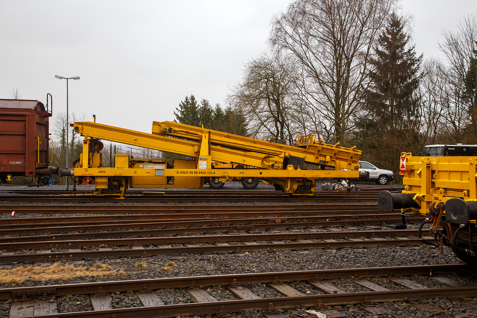Die Plasser & Theurer Beladestation BLS 2000 (BLS 40 – 2000) der HERING Bahnbau (Burbach) Schweres Nebenfahrzeug Nr. D-HGUI 99 80 9552 123-8, ex 97 19 26 502 57-8 ist am 13.03.2023 auf dem Betriebshof der Westerwaldbahn (WEBA) auf der Bindweide bei Steinebach/Sieg abgestellt.

Die Beladestation wurde 1993 von Plasser & Theurer unter der Fabriknummer 2161 gebaut.

Die BLS 2000 ist ein zweiachsiges, gleisfahrbares Gerät. Die BLS 2000 kann unter spannungsführenden Fahrleitungen eingesetzt werden. Sie kann mit MFS 38, 40, 100, BSW 2000 und 6000 gekoppelt werden. Der Boden des Aufnahmebandes und des Übergabebandes ist als steuerbares Band mit einer Förderbreite von 1.920 mm ausgebildet. An der Baustelle angekommen, ist eine Aufrüstzeit von ca. 3 Minuten nötig. Der Aufnahmetrichter wird auf eine Höhe von max. 1,15 m über SOK abgesenkt und das Übergabeband wird ausgefahren. Hiernach können die Schüttgüter (alter Gleisschotter, Planum etc.) mittels Laderaupe, Radlader oder Bagger über die BLS in die MFS oder BSW verladen werden. Die Förderbänder werden hydraulisch angetrieben. Der Antrieb des Hydraulikaggregates erfolgt durch einen luftgekühlten Deutz Dieselmotor vom Typ F5L912 mit einer Leistung von 64 kW.

TECHNISCHE DATEN:
Achsanzahl: 2
Eigengewicht: 22.600 kg
Länge über Puffer: 12.900 mm
Achsabstand: 8.000 mm
Laufraddurchmesser: 730 mm (neu)
Höchstgeschwindigkeit: 100 km
Kleinster befahrbarer Gleisbogen: R 120 m
Bremse: KE-GP
Handbremse: Ja