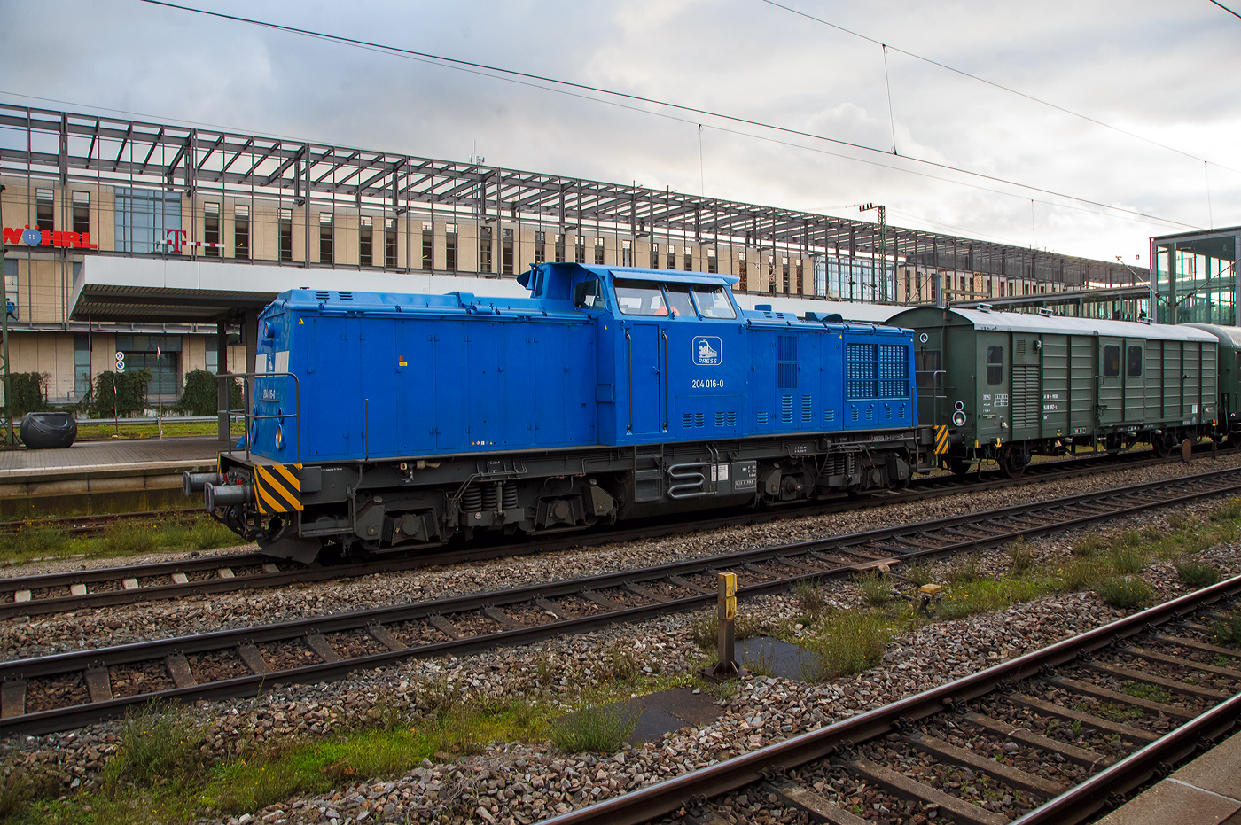 Die PRESS 204 016-0 alias 204 314-9 (92 80 1204 314-9 D-PRESS) fährt am 24.11.2022 mit einem Dienstzug durch den Hauptbahnhof Regensburg.

Die V 100.1 ost wurde 1970 LEW (VEB Lokomotivbau Elektrotechnische Werke „Hans Beimler“ Hennigsdorf) unter der Fabriknummer 12823 gebaut und als DR 110 314-2 an die Deutsche Reichsbahn geliefert. Im Bw Erfurt erfolgte 1983 der Umbau zur DR 115 314-7, dabei erhielt sie einen stärkeren KVD Motor vom Typ 12 KVD 18/21-AL4 des Herstellers VEB Kühlautomat Berlin-Johannistal. 

Typschlüssel 12 KVD 18/21-AL4  = 12 Zylinder Viertakt-Dieselmotor mit 180 mm Bohrung / 210 mm Hub, A = aufgeladener Motor, Bauform 5 mit Ladeluftkühler, mit einer Leistung von 883 kW (1.200 PS)

Zum 01.01.1984 erfolgten dann die Umzeichnung in DR 114 314-8, zum 01.01.1992 in DR 204 314-9 und zum 01.01.1994 in DB 204 314-9. Im November 2003 erfolgte die z-Stellung und im Mai 2011 die Ausmusterung und Verkauf an  ALS - ALSTOM Lokomotiven Service GmbH in Stendal. Bei der ALS in Stendal bekam sie einen neunen Caterpillar V-12-Zylinder-Viertakt-Dieselmotor mit Turboaufladung und Ladeluftkühlung vom Typ CAT 3512 DI-TA.

Typschlüssel CAT 3512 DI-TA = Bauart 3500, 12 Zylinder, Dieselmotor, Turbomotor mit Ladeluftkühlung. Motordaten: 170 mm Bohrung / 190 mm Hub, Hubraum 51.8 l, Nenndrehzahl 1.800 U/min, Leistung 932 kW (1.268 PS), Motorgewicht (trocken) 6.078 kg, Hersteller Caterpillar (CAT) Vertrieb in Deutschland über Zeppelin Power Systems.

Im Februar 2012 wurde die V100 an die PRESS - Eisenbahn-Bau- und Betriebsgesellschaft Pressnitztalbahn mbH in Jöhstadt verkauft, wo sie die Betreiberbezeichnung 204 016-0 bekam, wobei sie die NVR-Nummer 92 80 1204 314-9 D-PRESS hat.

Als Baureihe V 100 (ab 1970 DR 110) bezeichnete die Deutsche Reichsbahn vierachsige Streckendiesellokomotiven für den mittleren Dienst. Das Mitte der 1950er Jahre von der Deutschen Reichsbahn (DR) aufgestellte Diesellokprogramm zur Ablösung der Dampflokomotiven enthielt die Baureihen V 15, V 60, V 180 und V 240. Es fehlte jedoch eine Lokomotivbauart mit etwa 1.000 PS (ca. 700 kW) Leistung für den leichten bis mittleren Personen- und Güterzugdienst sowie den schweren Rangierdienst, die die Dampflokomotiven der Baureihen 38, 55, 57, 78 und 93 hätte ersetzen können. Diese Lücke sollte zunächst durch Import von auf der sowjetischen TGM3 basierenden Maschinen gefüllt werden. Als klar wurde, dass die Sowjetunion nicht im Stande sein würde, die Lokomotiven zu liefern, wurde 1963 mit der Entwicklung einer eigenen 10.00-PS-Diesellokomotive begonnen, wobei möglichst viele Teile der V 180 Verwendung finden sollten.

Als Ergebnis entstand beim Lokomotivbau Karl Marx Babelsberg eine vierachsige Diesellokomotive mit Mittelführerstand und hydraulischer Kraftübertragung. Das erste Baumuster von 1964 hatte noch den aus der V 180 bekannten 900-PS-Motor, das zweite Baumuster von 1965 erhielt bereits den 1.000-PS-Motor vom Typ 12 KVD 18/21 A-3 vom VEB Motorenwerk Johannisthal der Serie. Die beiden Baumuster wurden nicht von der Deutschen Reichsbahn übernommen. Sie wurden 1968 bei einem Großbrand im Raw Cottbus zerstört. 

Nachdem sich abzeichnete, dass die Serienfertigung aus Kapazitätsgründen beim Lokomotivbau Elektrotechnische Werke „Hans Beimler“ Hennigsdorf (LEW) stattfinden sollte, baute dieser 1966 eine weitere Musterlok (V 100 003). Diese dritte und älteste erhaltene Lokomotive befindet sich heute als Leihgabe des DB-Museums Nürnberg beim Förderverein Berlin-Anhaltische Eisenbahn in Lutherstadt Wittenberg und trägt die ursprüngliche Lackierung (creme mit grünen Streifen). Ein Jahr später begann die Serienfertigung, die Lokomotiven erhielten die Nummern V 100 004 bis 171.

Zum Einsatz auf Nebenstrecken mit geringerer Achslast wurde versucht, die Masse der Lokomotiven zu verringern. So wurde unter anderem auf das Stufengetriebe verzichtet. Damit konnte die Betriebsmasse auf 63 Tonnen gesenkt werden. In dieser Version wurden von 1969 bis 1978 696 Lokomotiven gebaut, die Erste als V 100 201, die Letzte dann schon mit neuer Baureihenbezeichnung als 110 896.

Die V 100 ersetzten in den folgenden Jahren fast alle Länderbahnlokomotiven im mittleren Leistungsbereich und kamen dabei vor fast allen Zugarten in der gesamten DDR zum Einsatz. Das letzte gebaute Exemplar mit 1.000 PS war die 1978 gebaute 110 896.

Insgesamt wurden 1146 Lokomotiven gebaut, 748 als V 100.1, 120 als V 100.2, 86 als V 100.4 und V 100.5 sowie 190 als V 100.2 und V 100.3 für den Export nach China (werksinterne Bezeichnungen der Varianten, nicht zu verwechseln mit den Baureihennummern).

Die Entwicklung endete mit der Baureihe 114 (DB BR 204) mit einem 12 KVD 18/21-AL4 und ab 1988 mit einem 12 KVD 18/21-AL5. Da die 1.200 PS auf Steilstrecken in den Mittelgebirgen durchaus noch zu wenig waren, wurden immer wieder Versuche mit weiterentwickelten Motoren und Getrieben gemacht. Zunächst wurden Motoren mit 1.400 PS (1029 kW) Nennleistung und zwei Kühlkreisläufen eingebaut, was dem Nummernschema der DR entsprechend zur Einordnung in die Baureihe 114 führte. Mit dieser Leistung waren die Motoren vorerst am Limit angelangt, eine Folge war die Neigung zu Kolbenfressern und insgesamt mehr Verschleiß sowie Störanfälligkeit war die Folge. Mit der Verfügbarkeit eines verbesserten Abgasturboladers konnte die Leistung auf 1.500 PS (1.100 kW) erhöht werden. Dieser 1,100-kW-Motor wurde 1983 zuerst in die schon mehrfach mit verbesserten Motoren ausgerüstete 110 203 und die 110 358 eingebaut. Solche Maschinen bildeten ab 1. April 1983 die Baureihe 115. Als nur noch 1100-kW-Motoren im Umbauprogramm eingebaut wurden, entschloss sich die Deutsche Reichsbahn im Herbst 1983, die umgebauten Lokomotiven in der Baureihe 114 zusammenzufassen. Die Reihenbezeichnung 115 sollte für geplante Neubaulokomotiven freigehalten werden. Der ab 1988 verwendete 12 KVD 18/21-AL5 hatte ein Zweikreis-Kühlsystem, eine neue Kurbelwelle und Zylinder und für jede Einspritzpumpe eine Kraftstoffpumpe. Dieser neue Motor wurde nachträglich auch in die schon vorher umgerüsteten Lokomotiven eingebaut. Insgesamt wurden zwischen 1983 und 1991 im Raw Stendal 65 Lokomotiven umgebaut.

Alle Lokomotiven im Betriebsbestand erhielten bei der Einführung des gemeinsamen Nummernplanes 1992 die Baureihenbezeichnung 204 und wurden am 1. Januar 1994 von der Deutschen Bahn übernommen. Die letzte 204 wurde im Mai 2009 ausgemustert. Weitere Maschinen wurden an Tochterunternehmen der Railion (heute: DB Cargo) verkauft. Heute fahren Lokomotiven dieser Baureihe auch in Bulgarien und Rumänien.

Technische Merkmale:
Die Lokomotive läuft auf zwei zweiachsigen Drehgestellen, die über je einen Drehzapfen angelenkt sind. Der Hauptrahmen, in den ersten Serien (bis zur V 100 103) mit Langträgern in Fischbauchform, stützt sich über Schraubenfedern mit Gleitplatten auf diesen Drehgestellen ab. Der Verzicht auf die Fischbauchträger verringerte die Masse um 1,8 Tonnen, was zur Tauglichkeit auch für Strecken mit 15 t Achslast führte.

Die Lokomotive besitzt einen Mittelführerstand. Im vorderen Vorbau sind der Dieselmotor und die Kühlanlage untergebracht. Im hinteren Vorbau haben Lüftergenerator, Lichtanlassmaschine, Schaltschrank 3, Luftgerüst, Luftbehälter, Batterien, der Heizkessel (oder entsprechende Vorwärmgeräte, Ballastgewichte sowie die Fahrzeugeinrichtung der Zugbeeinflussung und meist auch das Zugfunkgerät ihren Platz.

Im Fahrzeugrahmen unter dem Führerstand hängt das Strömungsgetriebe. Es ist über eine Gelenkwelle mit dem Motor verbunden. Das Getriebe hat einen Anfahr- und zwei Marschwandler sowie ein Wendegetriebe. Vom Getriebe erfolgt der weitere Kraftfluss über Gelenkwellen zu den Radsatzgetrieben. Die Radsätze eines Drehgestells sind über eine weitere Gelenkwelle miteinander verbunden. Links und rechts vom Getriebe sind die Kraftstofftanks angebracht.

Die Lokomotiven sind mit einer vierunddreißigpoligen Vielfach- und Wendezugsteuerung ausgerüstet. Deshalb wird die Drehzahl des Original-Dieselmotors elektromechanisch verstellt. Dazu können am Fahrschalter, der mit einem Trabant-Lenkrad betätigt wird, sechs Fahrstufen vorgewählt werden, die ein elektrischer Drehzahlversteller dann am Regler der Blockeinspritzpumpen einstellt. Die Lokomotive ist für eine Höchstgeschwindigkeit von 100 km/h zugelassen, die jedoch für DB-Lokomotiven auf 80 km/h herabgesetzt wurde.

TECHNISCHE DATEN:
Spurweite: 1.435 mm (Normalspur)
Achsformel: B'B'
Länge über Puffer: 14.240 mm
Drehzapfenabstand: 7.000 mm
Achsstand im Drehgestell: 2.300 mm
Raddurchmesser: 1.000 mm (neu)
Breite: 3.140 mm
Höchstgeschwindigkeit: 100 km/h 
Dienstgewicht: 68 t
Nennleistung: 932 kW (1.268 PS)
Hubraum: 51,7 Liter (Bohrung-Ø 170 x Hub 190 mm)
Leistungsübertragung: dieselhydraulisch
Anfahrzugkraft: 207 kN
Kleinste befahrbarer Gleisbogen: R 80 mm
Bremse: K-GPmZ
