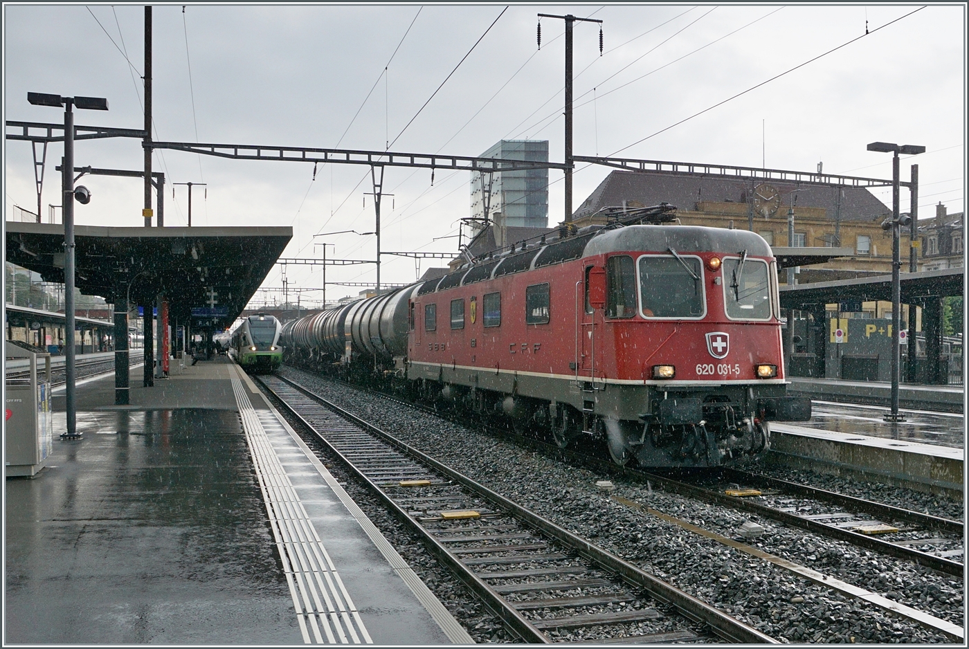 Die SBB Re 6/6 11631 (Re 620 031-5)  Dulliken  fährt während eines kurzen Regenschauers durch den Bahnhof von Neuchâtel. 

26. Juni 2024