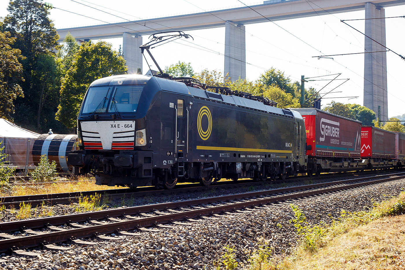 Die SIEMENS Vectron MS X4E – 664 / 193 664-0 (91 80 6193 664-0 D-DISPO) der BRCE - Beacon Rail Capital Europe (München) fährt am 21 September 2024 mit einem KLV-Zug durch Eiserfeld in Richtung Siegen. 

Die Multisystemlokomotive Siemens Vectron MS wurde 2017 von Siemens Mobilitiy in München-Allach unter der Fabriknummer 22244 gebaut. Sie wurde in der Variante A09 (Zulassungen für D / A / I) ausgeführt. Im Jahr 2022 erfolgte bie Siemens in München-Allach der Umbau in die Variante A22 und hat so die Zulassung für Deutschland, Österreich, die Schweiz, Italien und die Niederlande (D / A / CH / I / NL). So besitzt die Variante MS A22 folgende Zugsicherungssysteme: ETCS BaseLine 3, sowie für Deutschland (PZB90 / LZB80 (CIR-ELKE I)), für Österreich (ETCS Level 1 mit Euroloop, ETCS Level 2, PZB90 / LZB80), für die Schweiz (ETCS Level 2, ZUB262ct, INTEGRA), für Italien (SCMT) und die Niederlande (ETCS Level 1, ETCS Level 2, ATB-EGvv)

Die Lok wurde an die MRCE - Mitsui Rail Capital Europe GmbH in München ausgeliefert, seit September 2023 hat die Beacon Rail Metro Finance B.V. die Mitsui Rail Capital Europe B.V. (Amsterdam) und somit auch die Mitsui Rail Capital Europe GmbH im München übernommen, so firmiert sie nun als Beacon Rail Capital Europe GmbH, München (BRCE / DISPO).