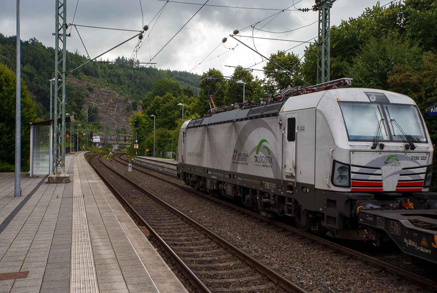 Die TXL eigene SIEMENS Vectron der TX Logistik AG, bisher hatte diese nur Loks angemietet. Die recht neue weiße TXL 7193 322 „Connected to Nature“ (91 80 7193 322-3 D-TXL) der TXL - TX Logistik AG (Troisdorf) fährt am 28 Juli 2025, mit einem KLV-Zug, durch den Bahnhof Kirchen (Sieg) in Richtung Betzdorf bzw. Köln.

Die SIEMENS Vectron MS (X4E) wurde 2024 von Siemens Mobility in München-Allach unter der Fabriknummer 23680 gebaut und am 31.03.2025 an die TXL ausgeliefert. Die mit 6.400 kW konzipierte Mehrsystemlok ist in der Variante A09-4f ausgeführt und hat so die und hat so die Zulassungen und entspr. Länderpakete für Deutschland, Österreich uns Italien (D / A / I).

Über TX Logistik AG
TX Logistik wurde 1999 als privates Eisenbahnverkehrsunternehmen gegründet und bietet mit Verbindungen in elf Ländern ein leistungsfähiges europäisches Netzwerk. Das Unternehmen verfügt über Tochtergesellschaften in der Schweiz, Österreich, Dänemark und Schweden sowie eine lokale Präsenz in Italien. In den Geschäftsbereichen Intermodal und Rail Freight entwickelt TX Logistik umfassende Schienenlösungen für kontinentale und maritime Verkehre sowie maßgeschneiderte Konzepte für konventionelle Fracht. Mit 650 Mitarbeitern und 8,6 Milliarden gefahrenen Tonnenkilometern erwirtschaftete das Unternehmen 2021 einen Jahresumsatz von 253 Millionen Euro. Seit Januar 2017 gehört TX Logistik zu 100 Prozent der Mercitalia Logistics S.p.A., einer Tochtergesellschaft der FS - Ferrovie dello Stato Italiane. Mittlerweile gehört das Unternehmen mit zu den Größten für den Schienengüterverkehr in Europa.

Das Unternehmen bietet den ganzen Umfang an Schienengüterverkehr, inklusive Containertransport und kombiniertem Verkehr an. Wichtigste Transportstrecken sind von den Häfen Hamburg, Bremerhaven, Rotterdam und Antwerpen nach Süddeutschland, Schweiz, Österreich und Italien.

TX Logistik setzt nun auf eigene Vectron Loks:
Anfang Oktober 2024 hat die TX Logistik AG ersten drei von 40 modernen Vectron-Lokomotiven des Herstellers Siemens Mobility aufs Gleis gesetzt, die das zur Mercitalia Logistics (FS Italiane Group) gehörende Schienenlogistikunternehmen im Mai 2023 bestellt hatte. Die Erweiterung der Fahrzeugflotte ist für TX Logistik eine wichtige Voraussetzung, um im intermodalen und grenzüberschreitenden Schienengüterverkehr weiter zu wachsen. Die neuen Lokomotiven werden vor allem auf dem Brenner- und dem Schweiz-Korridor eingesetzt, den strategisch wichtigen Nord-Süd-Achsen in Europa.

Beide Korridore sind stark frequentiert und stellen hohe Anforderungen an die eingesetzten Lokomotiven – von der Zugkraft über die Stabilität bis hin zur grenzüberschreitenden Systemkompatibilität. TX Logistik hat dazu die Maschinen mit verschiedenen Länderpaketen bestellt. 20 Vectron erhalten das Länderpaket für den Betrieb in Deutschland, Österreich, Schweiz, Italien und den Niederlanden (D-A-CH-I-NL) und sollen bis Anfang 2025 übergeben werden. Die Auslieferung der 20 Lokomotiven mit der Ausstattung für den deutsch-österreichisch-italienischen Korridor (D-A-I) soll bis zum Jahresende 2025 erfolgen.

Die Entscheidung für den Kauf der Vectron-Lokomotiven unterstreicht zugleich das Bestreben von TXLogistik, Schienengüterverkehre als umweltfreundliche und effiziente Alternative zum Straßentransport weiter voranzutreiben. Um dies zu unterstreichen und gleichzeitig für den Einstieg in den intermodalen Transport zu werben, hat die erste der drei Vectrons, die im Zughotel in Braunschweig übergeben wurden, eine spezielle Lok-Beklebung mit dem Schriftzug „Start now (Nature). Driven by Green Passion“ erhalten.

Die neuen Loks bieten mit ihrer Flexibilität und Leistungsfähigkeit ideale technische Voraussetzungen, um den steigenden Anforderungen des europäischen Güterverkehrs gerecht zu werden. Mit der modernen Vectron-Flotte, so TX Logistik, sei man mittelfristig nun in der Lage, die Kapazitäten auf dem Brenner- und dem Schweiz-Korridor deutlich zu erhöhen sowie die Effizienz und Zuverlässigkeit im Schienengüterverkehr weiter zu verbessern.