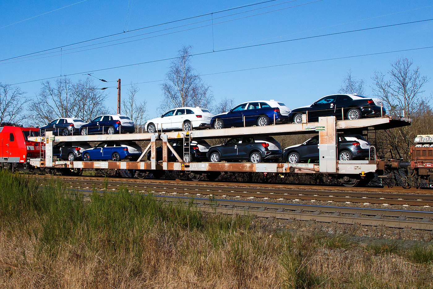 Doppelstock-Autotransportwagen 23 80 4351 950-9 D-ATG, der Gattung Laaes 556, der DB Cargo Logistics GmbH (ex DB Schenker ATG) am 07.02.2023 im Zugverband bei einer Zugdurchfahrt in Wilnsdorf-Rudersdorf.

Der Wagen wurde 1992 Waggonbau Niesky gebaut.

Die Waggons haben zwei Ladeebenen und können je nach Bauart mit 9 bis 14 Mittelklasse-Pkw beladen werden. Die Waggons sind europaweit einsatzfähig und wurden gezielt für den internationalen Transport von PKW entwickelt. Zur Be- und Entladung der oberen Ladeebene an Kopframpen können die Wagenenden aus der Transportstellung in die sogenannte Rampenstellung abgesenkt beziehungsweise angehoben werden. Des Weiteren können die Wagenenden der oberen Ladeebene in die Beladestellung angehoben werden. Hierdurch wird die maximale Durchfahrtshöhe für die Be- und Entladung der Fahrzeuge auf der unteren Ladeebene realisiert.

TECHNISCHE DATEN:
Gattung: Laaes (Bauart 556)
Spurweite: 1.435 mm
Anzahl der Achsen: 4
Länge über Puffer : 27.000 mm
Achsabstand: 22.300 mm (9.000 / 4.300 / 9.000 mm)
Laufraddurchmesser: 840 mm (neu)
Ladelänge : 26.100 mm (unten) / 26.500 mm (oben)
Höchstgeschwindigkeit: 100 km/h (120 km/h leer)
Eigengewicht: 28.800 kg
Nutzlast: 24 t ab Streckenklasse A, unten max. 13 t / oben max. 11 t
Kleinster befahrb. Gleisbogenhalbmesser: 80 m
Bremse: KE-GP-A (LL)
Intern. Verwendungsfähigkeit: RIV