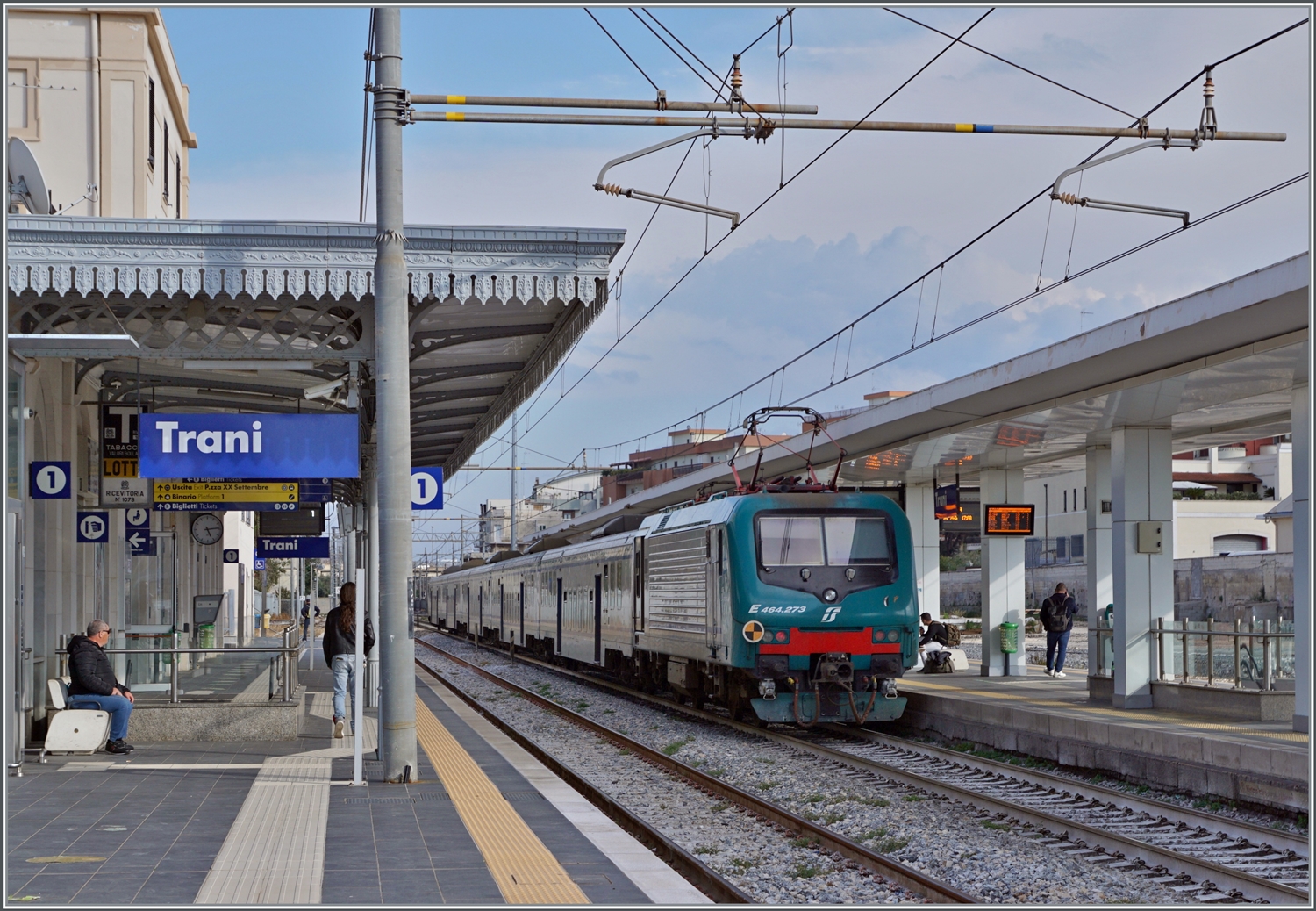 Ein FS Trenitalia Regionalzug in Richtung Bari hält in Trani. Trotz der vielen neuen Fahrzeuge sind hin und wieder weiterhin älter Züge im Einsatz, wie dieser FS Tpy 73 Niederflurzug (Carrozza vicinale a piano ribassato) in XMPR Lackierung mit einem npBD an der Spitze und vier nB Wagen sowie der schiebenden FS Trenitalia E 464 273.

20. April 2023