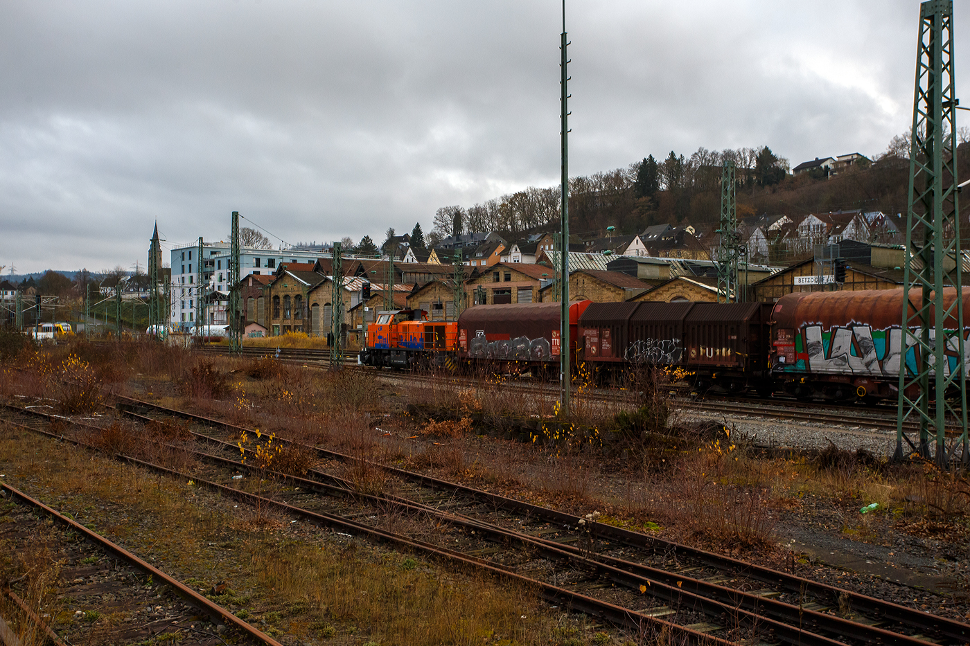 Geführt von der KSW 44 (92 80 1271 004-4 D-KSW), eine MaK G 1000 BB, fährt am 04 Dezember 2025 die KSW (Kreisbahn Siegen-Wittgenstein), im Sandwich mit einem sehr langen und schweren Coilzug, vom Rangierbahnhof Betzdorf/Sieg in Richtung Herdorf zum KSW-Rangierbahnhof (Betriebsstätte FGE - Freien Grunder Eisenbahn) nun los. Hinten (nicht im Bild) ist die nachschiebende KSW 42 bzw. 277 902-3 (92 80 1277 902-3 D-KSW) eine Vossloh MaK G 1700 BB. 

Die Fuhre geht ja über die, nicht elektrifizierte, eingleisige KBS 462 „Hellertalbahn“, da nur eine Güterverkehrsfahrt zwischen den Personenverkehr der RB 96 passt, fährt die KSW lieber eine lange Fuhre im Sandwich. Für eine Lok wäre die Anhängelast eines solchen langen beladenen Coilzuges zu hoch. In Herdorf auf dem Rangierbahnhof der KSW, werden Züge in mehren Teile aufgeteilt und gehen dann über die KSW eigene Strecke NE 447 (ehem. Freien Grunder Eisenbahn nach Neunkirchen-Salchendorf (ehemals Pfannenberger Einigkeit) zu den Produktionshallen der EMW Stahl Service GmbH, ein Geschäftsbereich der SCHÄFER WERKE Gruppe. 

Schon heute werden so dorthin über 300.000 Tonnen Stahl pro Jahr über die Schiene angeliefert, zukünftig sind sogar 600.000 Tonnen geplant.