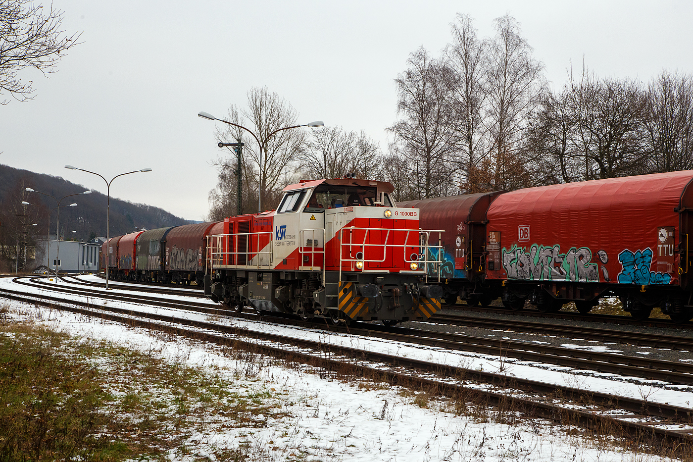 Güterverkehr gibt es noch in Herdorf....
Die KSW 47 (92 80 1271 027-5 D-KSW), ex D 2 der HFM, eine Vossloh G 1000 BB der KSW (Kreisbahn Siegen-Wittgenstein), fährt am 24.01.2023 auf dem KSW Rbf Herdorf (Betriebsstätte Freien Grunder Eisenbahn - NE 447). Gleichdrauf geht es aufs DB Gleis der Hellertalbahn (KBS 462 / Strecke-Nr. 2651). Nur nicht in Richtung Betzdorf, denn der Streckenanschnitt Herdorf – Betzdorf ist bis min. Ende April gesperrt, so muss die KSW den Umweg über Haiger fahren. Wobei hier als Lokzug ist es nur der Umweg und der entsprechende Mehrverbrauch an Kraftstoff, aber für den Güterverkehr ist noch die Streckenklasse sehr entscheidend und die beträgt bei dem Streckenanschnitt Herdorf – Haiger nur CE (anstatt D4 zwischen Betzdorf und Herdorf). Bei CE beträgt die Radsatzlast max. 20 t bei D4 aber 22,5 t. Dadurch kann ein Coil weniger geladen werden, da man nicht gerademal Coils vierteln kann, ergibt sich daraus ein bis zu 35% geringeres Ladegewicht und ein Mehraufwendung von Waggons. 
