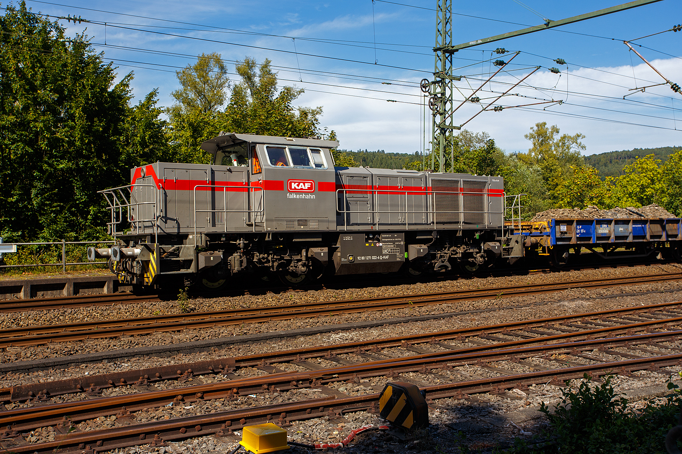 Nun drückt die 271 022-6 „Charlotte“ (92 80 1271 022-6 D-KAF) eine Vossloh/MaK G 1000 BB der KAF Falkenhahn Bau AG. ex MRCE bzw. ex HGK DH 49, am 26 August 2025 den mit Aushub beladenen Niederbordwagen-Zug (zweiachsiger Flachwagen NS Gattung Klmos 702 der Vermietungsfirma Railpro), von der Baustelle im Bf Scheuerfeld/Sieg ca. 3 km nach Betzdorf/Sieg. Beim Rbf Betzdorf befindet sich die Umladestation, hier wird der Aushub von Baggern abgeladen und zwischengelagert. 