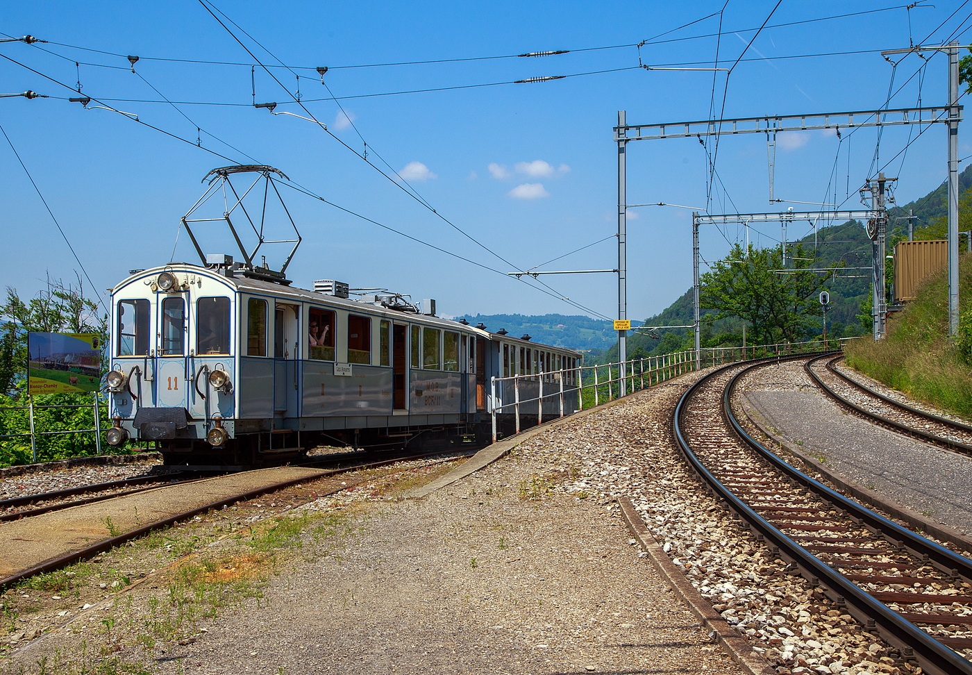 Pfingsten 2023 (Samstag 27. bis Montag 29. Mai 2023) fand bei der Museumsbahn Blonay–Chamby das Schweizer Dampffestival 2023 / Festival suisse de la Vapeur 2023 statt.

Der ex MOB BCFe 4/4 11 mit dem vierachsigen Personenwagen MOB BC 22 erreichen am 27.05.2023 den Bahnhof Chamby.

Der Triebwagen mit 2. und 3. Klassen- sowie Gepäckabteil wurde 1905 von der Schweizerischen Industrie-Gesellschaft (SIG) in Neuhausen am Rheinfall hergestellt und mit einer elektrischen Ausrüstung von der Elektrizitätsgesellschaft Alioth versehen. Der TW Nr. 11 ist der letzte erhaltene der Serie (von 14 Stück) und sogar als BCFe 4/4 11 betriebsfähig. Er ist Eigentum der Museumsbahn. Der vierachsigen Personenwagen MOB BC 22 wurde bereits 1902 von SIG gebaut. Der TW Nr. 11 ist der letzte erhaltene der Serie (von 14 Stück) und sogar als BCFe 4/4 11 betriebsfähig. Er ist Eigentum der Museumsbahn.

Die BCFe 4/4 7 bis 20 sind bzw. waren elektrische Meterspur-Triebwagen. Sie wurden zwischen 1904 und 1906 von der MOB (Montreux–Berner Oberland-Bahn, französisch Chemin de fer Montreux Oberland) beschafft. Diese Triebfahrzeugserie ist mit vierzehn Fahrzeugen die größte, die bis heute von der Montreux–Berner Oberland-Bahn beschafft wurde. Allerdings waren nur dreizehn Triebwagen gleich, einer hatte eine abweichende elektrische Ausrüstung von MFO. Verwandt mit diesen sind auch die beiden CFZe 4/4 1001 und 1002, welche sich nur im Kastenaufbau unterscheiden. Rahmen, Untergestelle und elektrische Ausrüstung sind gleich. Beide Triebwagenbaureihen wurden von SIG hergestellt und mit einer elektrischen Ausrüstung von der Elektrizitätsgesellschaft Alioth versehen, mit Ausnahme der Triebwagen BCFe 4/4 12 und CFZe 4/4 1002, die eine elektrische Ausrüstung von der Maschinenfabrik Oerlikon (MFO) erhielten.

Geschichte:
Für die Eröffnung des Bahnstrecken-Teilstückes Montbovon–Château-d'Oex–Gstaad im Jahre 1904 und Gstaad–Zweisimmen im Jahre 1905 stieg der Bedarf an Fahrzeugen bei der MOB an. Die entsprechenden Fahrzeuge wurden in den Jahren 1902 und 1903 bestellt. Insgesamt ging es dabei um eine Beschaffung von 16 Triebwagen, 21 zweiachsigen Personenwagen und 42 Güterwagen. Bei den 16 Triebwagen handelte es sich um die 14 BCFe 4/4 7 bis 20 und die beiden CFZe 4/4 1001 und 1002.

Technik:
Die Fahrzeuge hatten einen verblechten Holzkasten, der auf einem genieteten Stahlrahmen ruhte. Die vierpoligen eigenventilierten Gleichstrom-Motoren wurden als Einzelachsantriebe in den beiden zweiachsigen Drehgestellen ausgeführt. Über einen geschlossenen Tatzlager-Antrieb mit zweiteiligen elastischen Zahnrädern und einer Übersetzung (bei Ablieferung) von 1:4,33 wurde die Kraft auf die Achse mit Triebrädern von 860 mm Durchmesser übertragen. Bei 700 Volt an der Motorenklemme entwickelte jeder Motor an der Welle eine Stundenleistung von 65 PS (48 kW). Zusammen leisteten die vier Motoren somit 260 PS (192 kW).

Die Steuerung der Motoren erfolgte über einen Direktkontroller mit zehn Fahr- und fünf Bremsstufen. An den Motorenklemmen lag je nach Fahrstufe die volle Fahrleitungsspannung an. Es ist bereits beim Fahrzeugbau eine elektrische Widerstandsbremse eingebaut worden. Als Triebwagen- und Zugbremse wurde eine Vakuum-Bremse der Bauart Hardy eingebaut, die auf alle vier Achsen wirkte. Zusätzlich war als Hand- bzw. Feststellbremse eine Handspindelbremse sowie eine von der Fahrleitung gespeiste Magnetschienenbremse vorhanden. Die Fahrzeugbedienung erfolgte stehend.

Die anfängliche Höchstgeschwindigkeit von 45 km/h, wurde später auf 50 km/h erhöht.

Die Fahrzeuge besaßen gegenüber den Vorgängerfahrzeugen ein größeres Gepäckabteil, dafür ein kleineres 3.-Klasse-Abteil mit 16 Sitzplätzen auf Holzbänken. Die beiden 2.-Klasse-Abteile waren als geschlossene Seitengangabteile ausgeführt und hatten zwölf gepolsterte Sitzplätze. Im 6 m² großem Gepäckabteil gab es zehn Notsitze. Auch eine Toilette war vorhanden.

Eine Vielfachsteuerung war nicht vorhanden. Die Triebwagen wurden vor allem anfänglich viel in Mehrfachtraktion eingesetzt. Für die Kommunikation zwischen mehreren Triebfahrzeugen war eine Klingeleinrichtung eingebaut, durch die sich das Fahrpersonal mit festgelegten Zeichen verständigen konnte.

Die beiden 1908 nachbeschafften BCFe 4/4 21I und 22I waren praktisch baugleich, sie wogen mit 28 Tonnen 400 kg mehr als der Durchschnitt der früher gelieferten Fahrzeuge. Diese Triebwagen sind nicht zu verwechseln mit den später mit den gleichen Nummern bezeichneten Diensttriebwagen Xe 4/4 21II und 22II die aus den Triebwagen BFZe 4/4 1004 und 1005 hergerichtet wurden.

Umbauten
In den Jahren 1925 bis 1929 wurde bei den vier Triebwagen (7, 8, 10 und 11) die Motoren neu gewickelt und eine Fremdventilation der Fahrmotoren eingebaut sowie die Übersetzung auf 1:3,23 geändert. Dadurch stieg die Stundenleistung auf 340 PS und auch die Fahrgeschwindigkeit. Die entsprechenden umgebauten Triebwagen konnten nun zusammen mit den ursprünglich als BFZe 4/4 23–26 und den ursprünglich als CFZe 4/4 27–28 bezeichneten Triebwagen in Mehrfachtraktion eingesetzt werden. Zwischen 1965 und 1968 wurde diese Fremdventilation wieder ausgebaut. Im Jahr 1964 erhielt auch der Triebwagen 18 eine Fremdventilation, auch hier stieg die Stundenleistung auf 340 PS. Fahrzeuge mit eingebauter Fremdventilation waren rund 1 Tonne schwerer.

Im Jahr 1956 erfolgte eine Umzeichnung infolge Aufhebung der 3. Klasse in ABFe 4/4, 1962 folgte die Umzeichnung in ABDe 4/4.

Der Triebwagen ABDe 4/4 11 erhielt für das 75 Jahr-Jubiläum der Montreux–Berner Oberland-Bahn im Jahr 1976 einen Neuanstrich in den ursprünglichen Farben und mit den alten Anschriften sowie der alten Bezeichnung BCFe 4/4. 1993 wurde der Triebwagen in Chamby-Musée (Chaulin) stationiert. Im Jahr 2000 erfolgte die Abgabe an die Museumsbahn Blonay–Chamby (BC) die ihn wieder betriebsfähig aufarbeitete. Zwischen 2003 und 2004 erfolgte eine Totalrevision des Untergestelles und der Drehgestelle. Zwischen 2008 und 2012 erfolgte eine Totalrevision des Wagenkastens mit einem entsprechenden Neuanstrich.

TECHNISCHE DATEN:
Fahrzeugbezeichnung: BCFe 4/4, später ABFe 4/4, ABDe 4/4 
Anzahl Fahrzeuge: 14
Spurweite: 1.000 mm (Meterspur)
Achsanordnung: Bo'Bo'
Länge über Puffer: 14.210 mm
Länge Wagenkaten: 13.190 mm
Höhe: 3.340 mm (Dachoberkannte)
Drehzapfenabstand: 8.610 mm
Achsabstand im Drehgestell : 1.780 mm
Treibraddurchmesser (neu): 860 mm
Fußbodenhöhe: 1.205 mm
Dienstgewicht: 29 t
Höchstgeschwindigkeit: 50 km/h
Stundenleistung: 260 PS (4 x 48 kW =192 kW), Zwischenzeitlich mit Fremdventilation 340 PS (252 kW)
Anzahl der Fahrmotoren: 4
Getriebeübersetzung: 1:3,24
Sitzplätze: 12 in der 2. Klasse / 16 in der 3. Klasse 
Ladefläche Gepäckraum: 6 m² (2t)
Stromsystem: 850 V DC
Stromabnehmer: 1 Lyrabügel und 1 Scherenstromabnehmer

Quellen: Museumsbahn BC, x-rail.ch und wikipedia