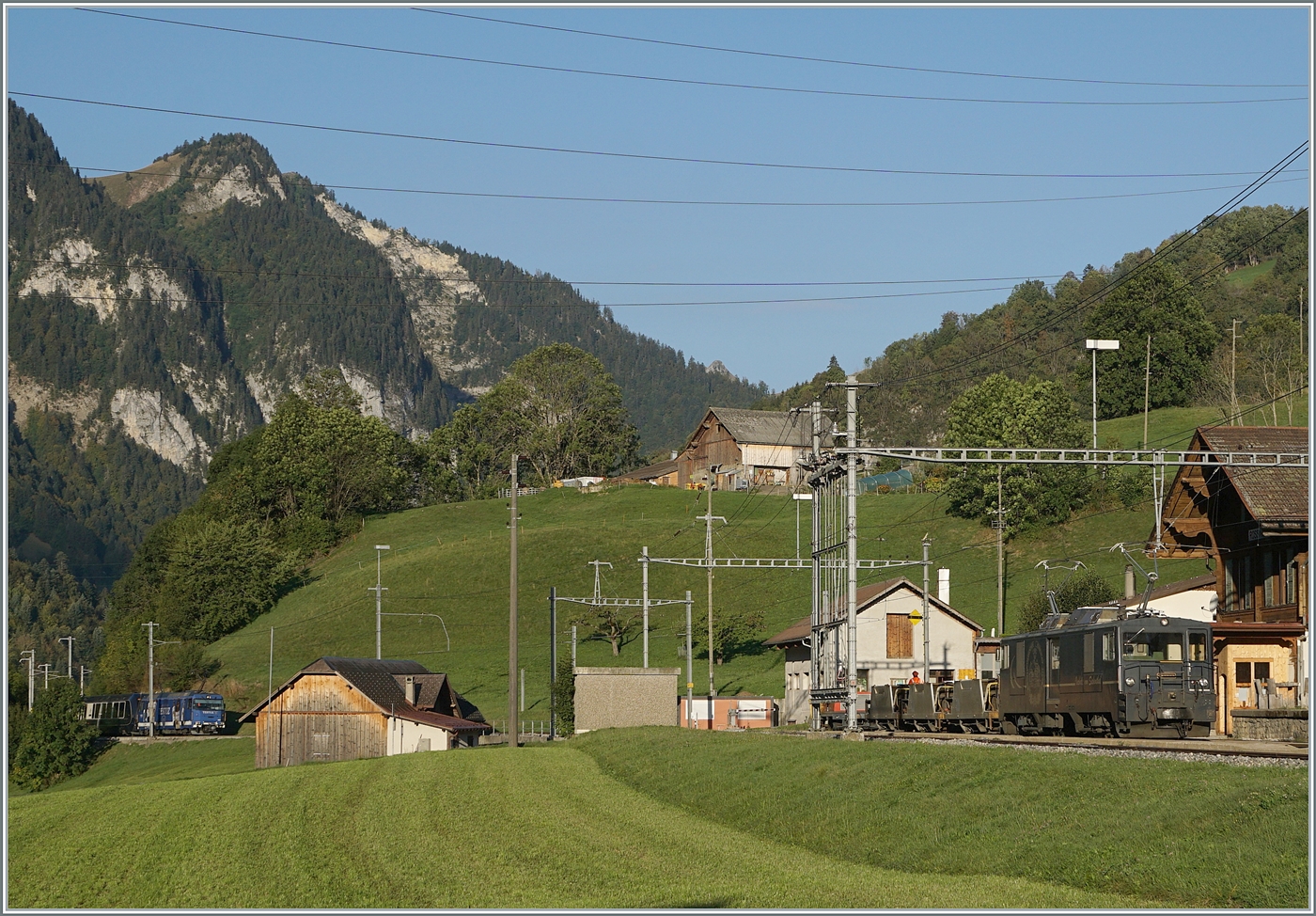 Rossinière mit der GDe 4/4 6002 die mit ihrem Schotterzug auf die Überholung des GoldenPass Express wartet, der ganz links im Bild auch schon auftaucht. 
29. Sept. 2023