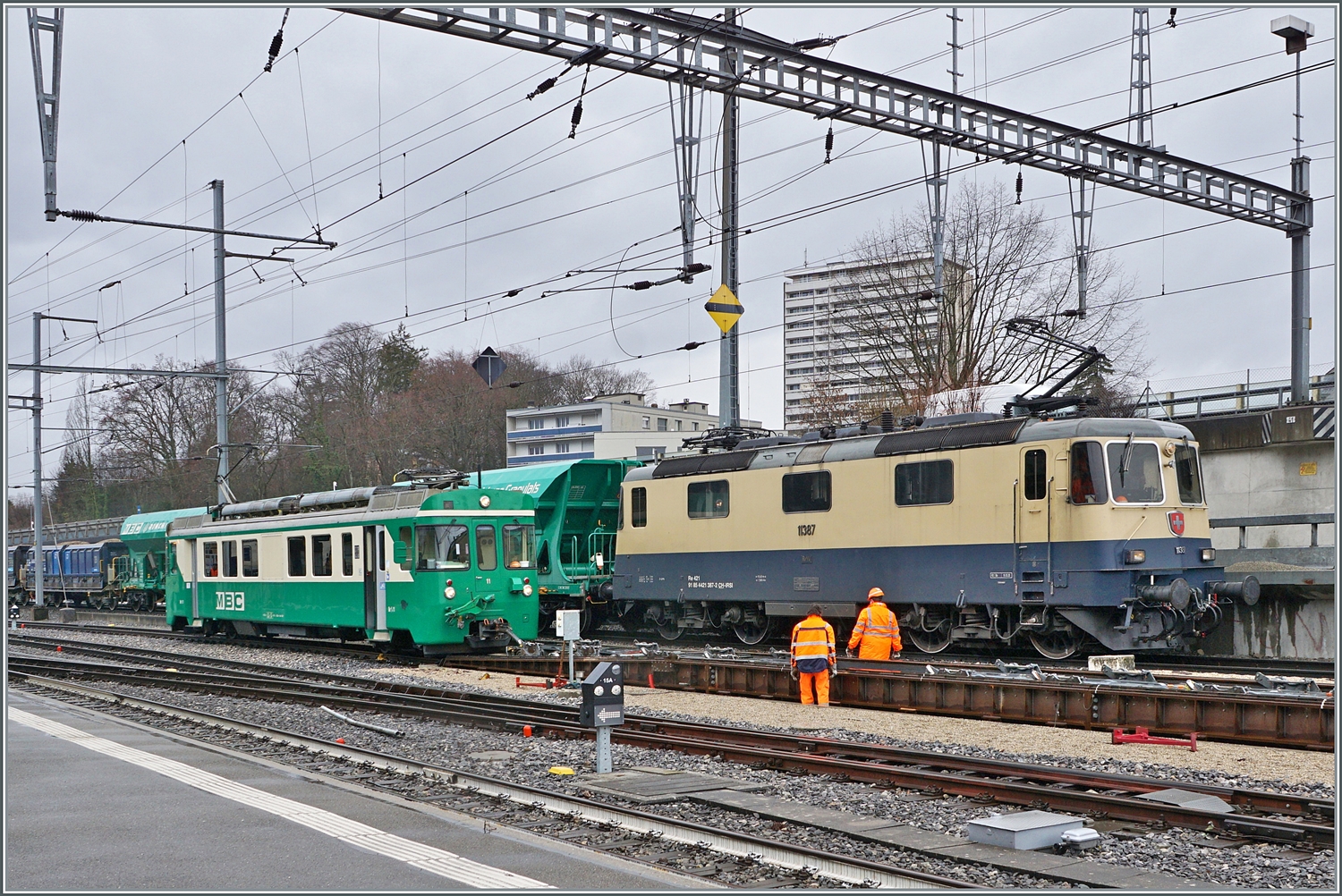 W�hrend die IRSI/IGE  Rheingold  Re 4/4 II 11387 (Re 421 387-2) in Morges ihren Kieszug �ber die Rollbockgrube schiebt, rangiert der BAM MBC Be 4/4 11 Rollb�cke.

22. Feb. 2024