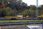 Ein Drehgestell-Flachwagen, Nummer unbekannt, der Gattung Res als Kran-Schutzwagen gegenlastseitig, u. a, beladen mit Werkstattcontainer, kleine Traversen, Anschlagmittel und sonstiges Zubehör/Equipment, sowie rechts der vierachsige Gegenlastwagen D-HGUI 99 80 9310 032-4 auf der einen Seite mit dem abgelegten Gegengewicht des 150 t Gleis- und Eisenbahndrehkran (EDK) KIROW Multi Tasker KRC 1200, D-HGUI 99 80 9419 041-5 „IDEFIX“ der HERING Bahnbau GmbH und auf der anderen Seite stützt, sich hier in der Transportstellung, das Gegengewicht-Teleskop hydraulisch auf dem Gegenlastwagen ab.

Abgestellt am 19 Oktober 2025 im Rbf Betzdorf/Sieg.